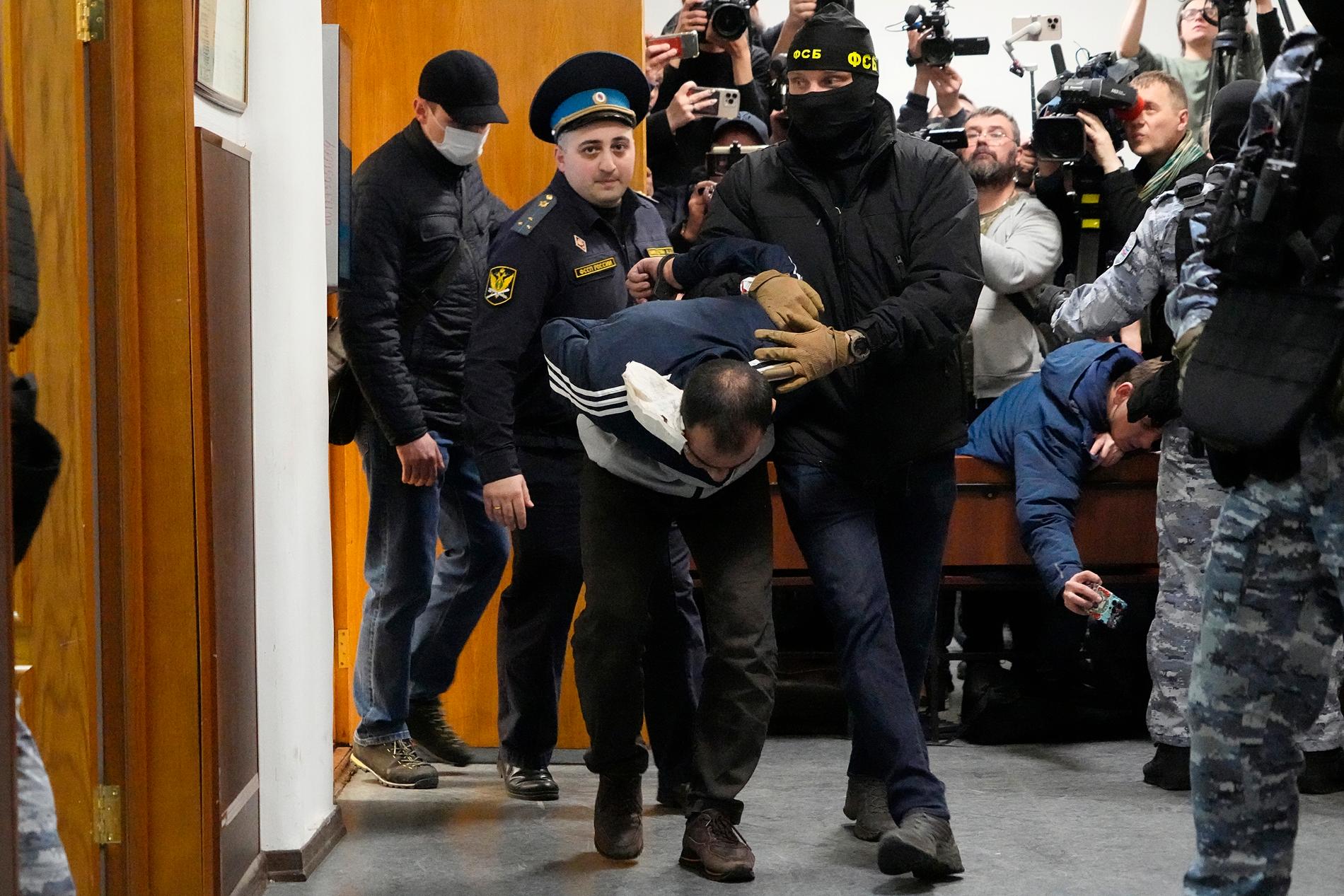 Den misstänkte terroristen Saidakrami Murodali Ratjabalizoda förs genom domstolsbyggnaden av polis och FSB. Han har ett stort bandage på huvudet efter att ha setts få sitt öra avskuret i ett filmklipp.