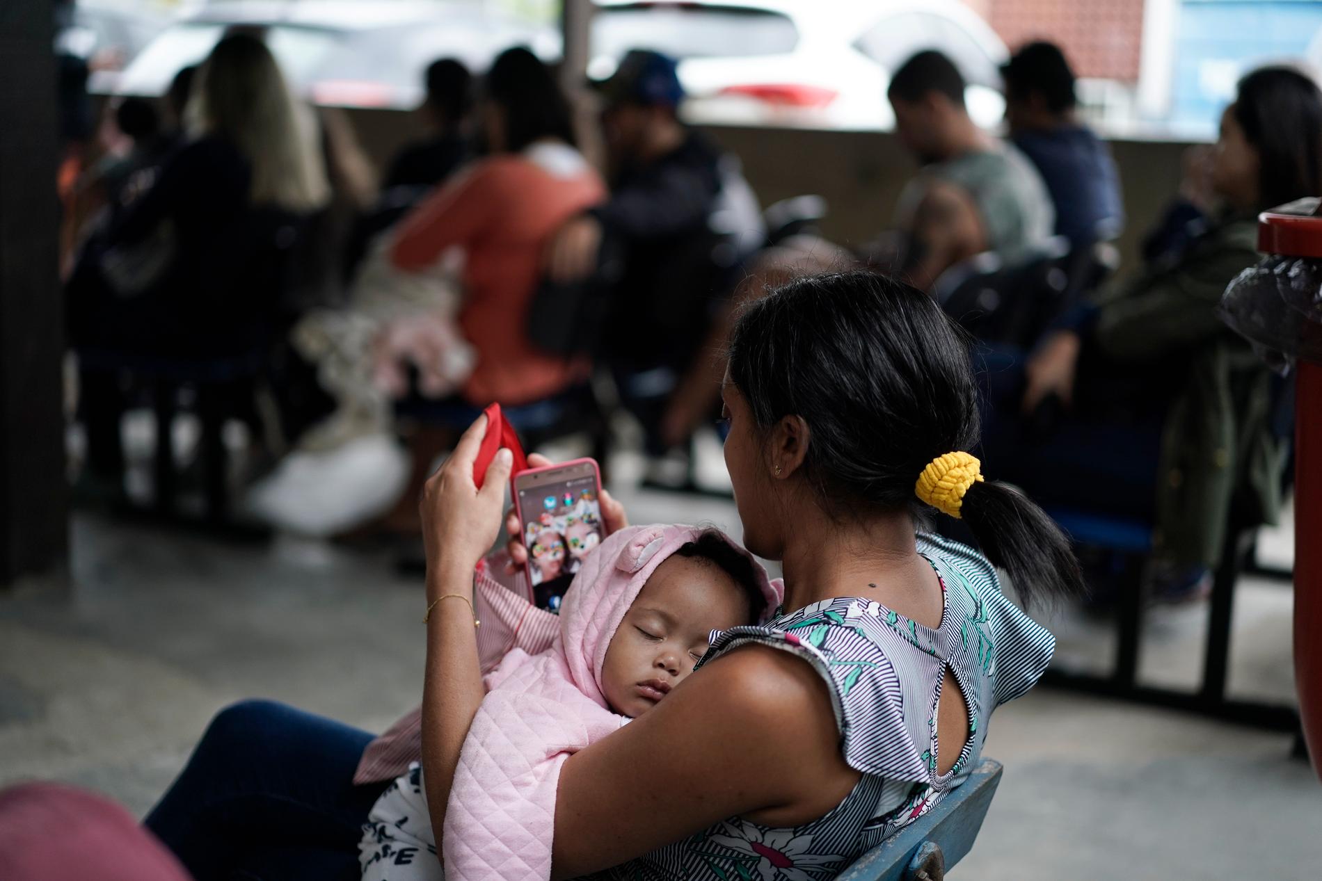 En mor vaggar sitt barn i väntan på vaccinering i brasilianska Rio de Janeiro i augusti i år.