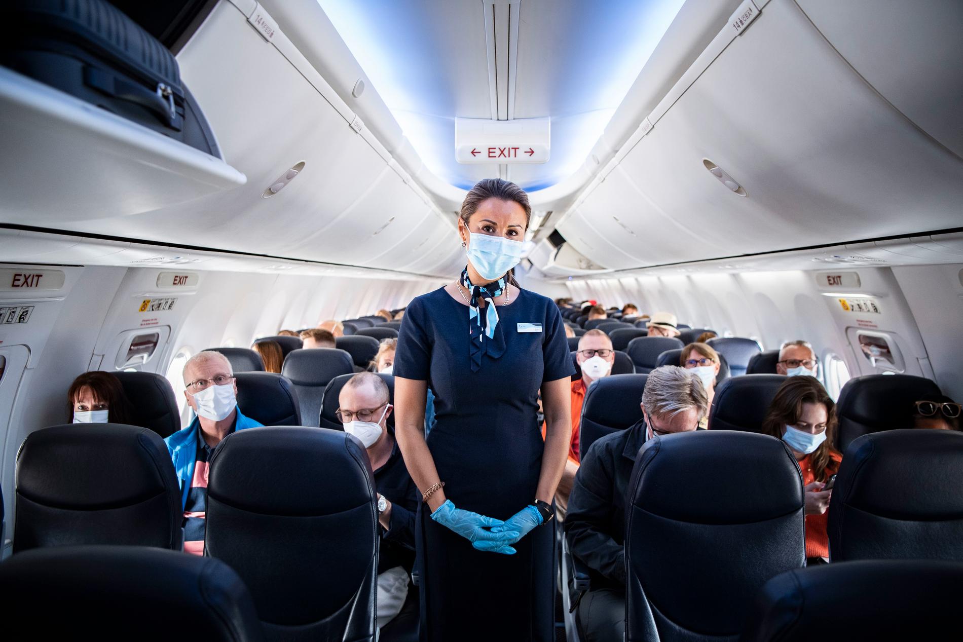 Flygvärdinna med munskydd och plasthandskar ombord på planet. 