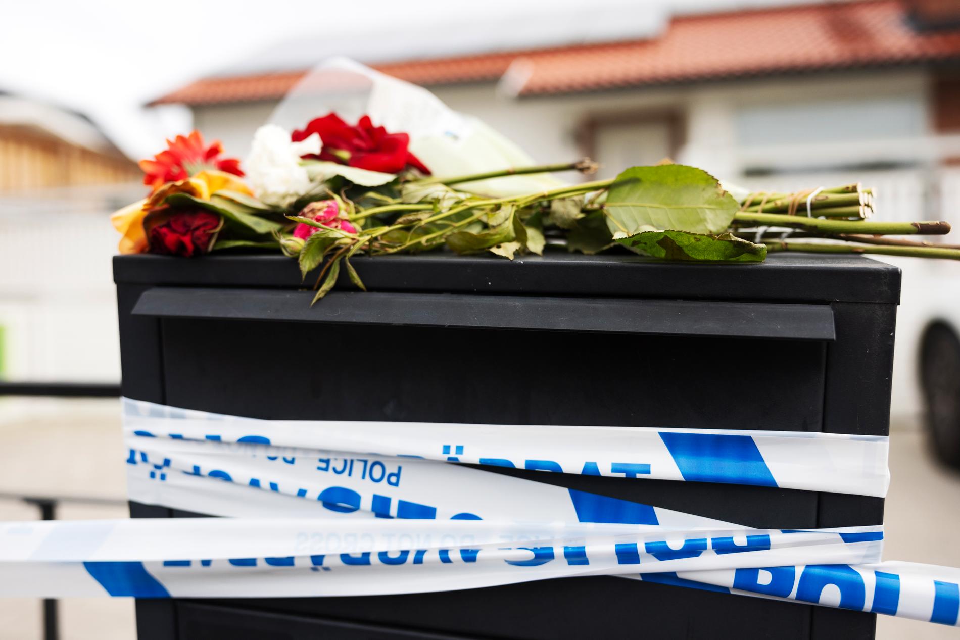 Våldsdåden skakar grannskapet. En brevlåda får hålla upp polisens avspärrningsband. Någon har lagt dit blommor. 