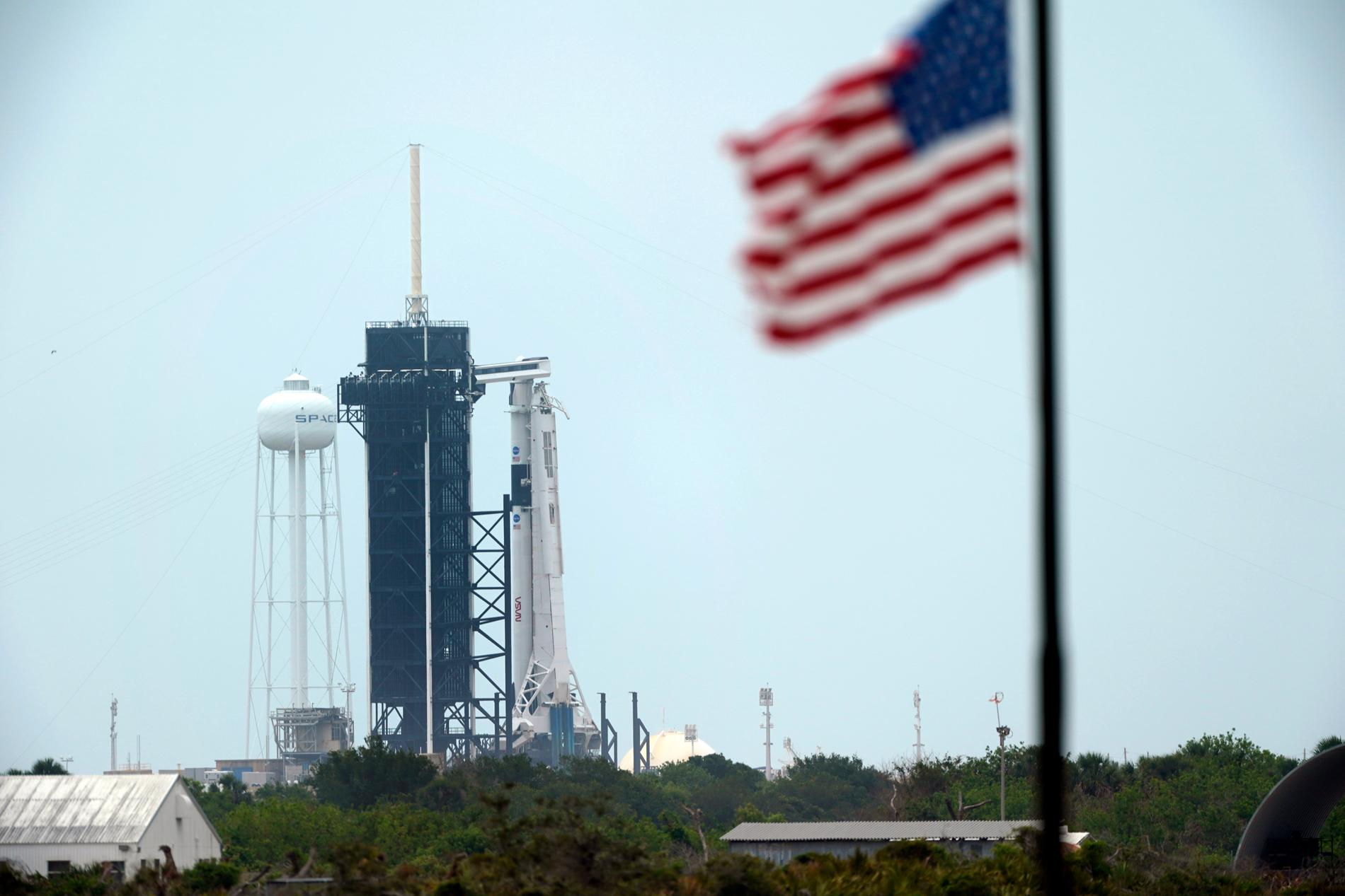 Den startklara Falcon 9-raketen från Space X, med besättningskapseln Crew Dragon högst upp, till höger om det svarta tornet på Kennedy Space Center.