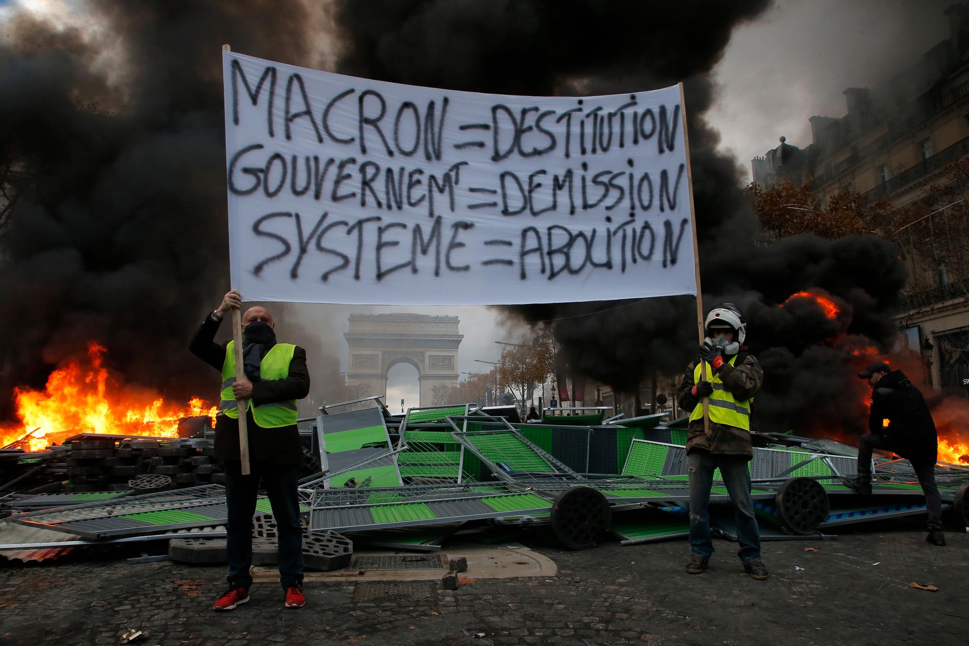 Demonstranter med en banderoll med slagord mot Frankrikes president Emmanuel Macron.
