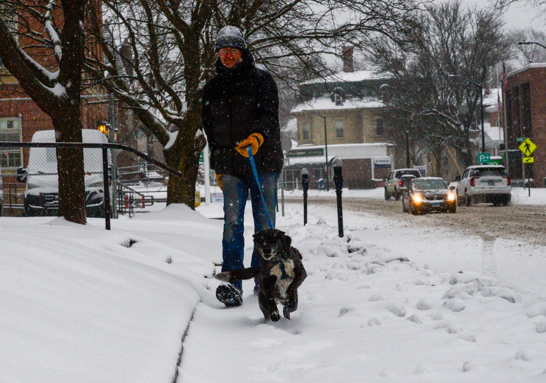 Man är ute och rastar hunden i snöfallet i New England. 