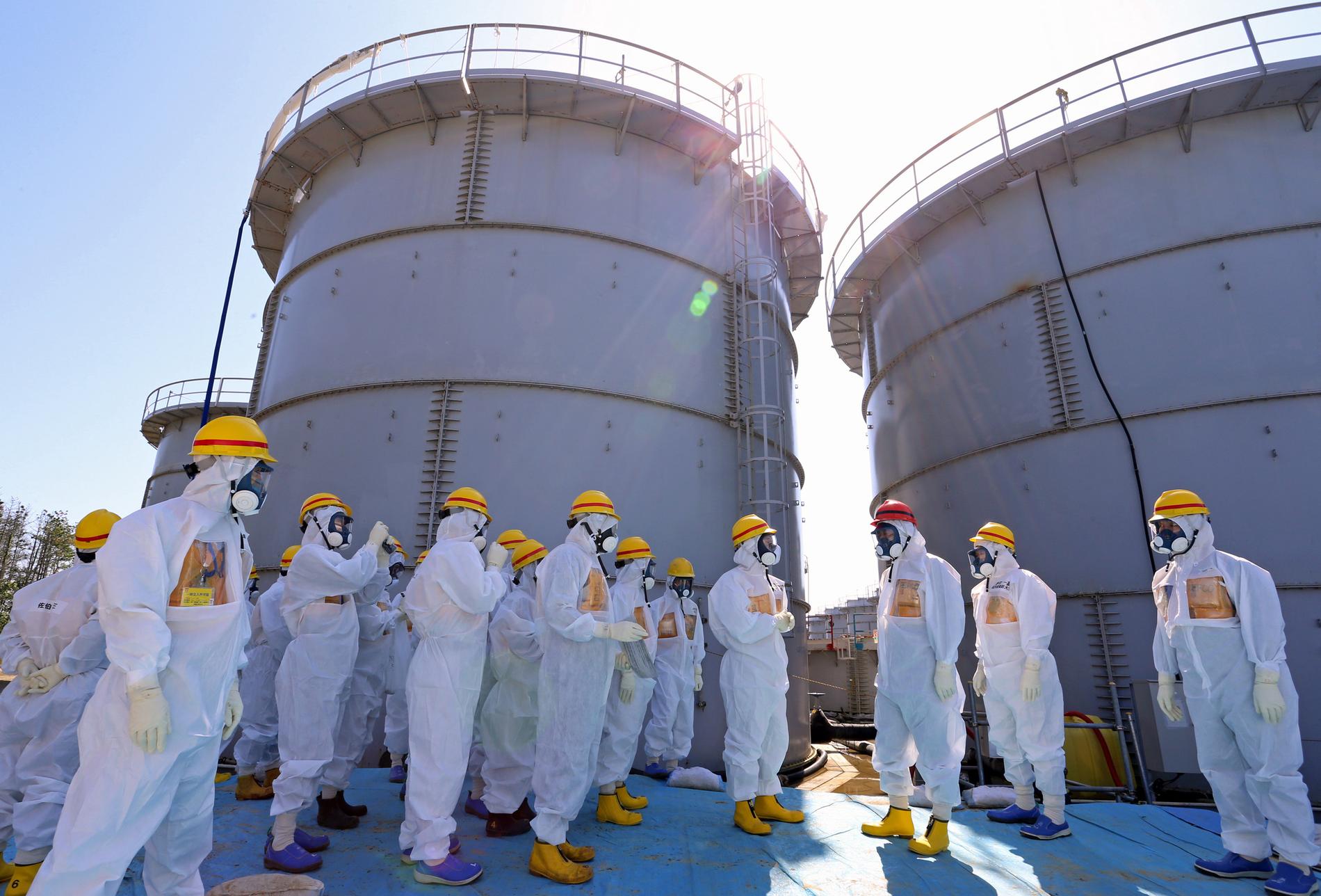 En av tusentals behållare av förorenat vatten vid Fukushimas kärnkraftverk i Japan (här med Japans premiärminister Shinzo Abe, röd hjälm). Nu öppnar regeringen och energibolaget som äger kärnkraftverket för att börja släppa ut det förorenade vattnet i havet. Arkivbild.