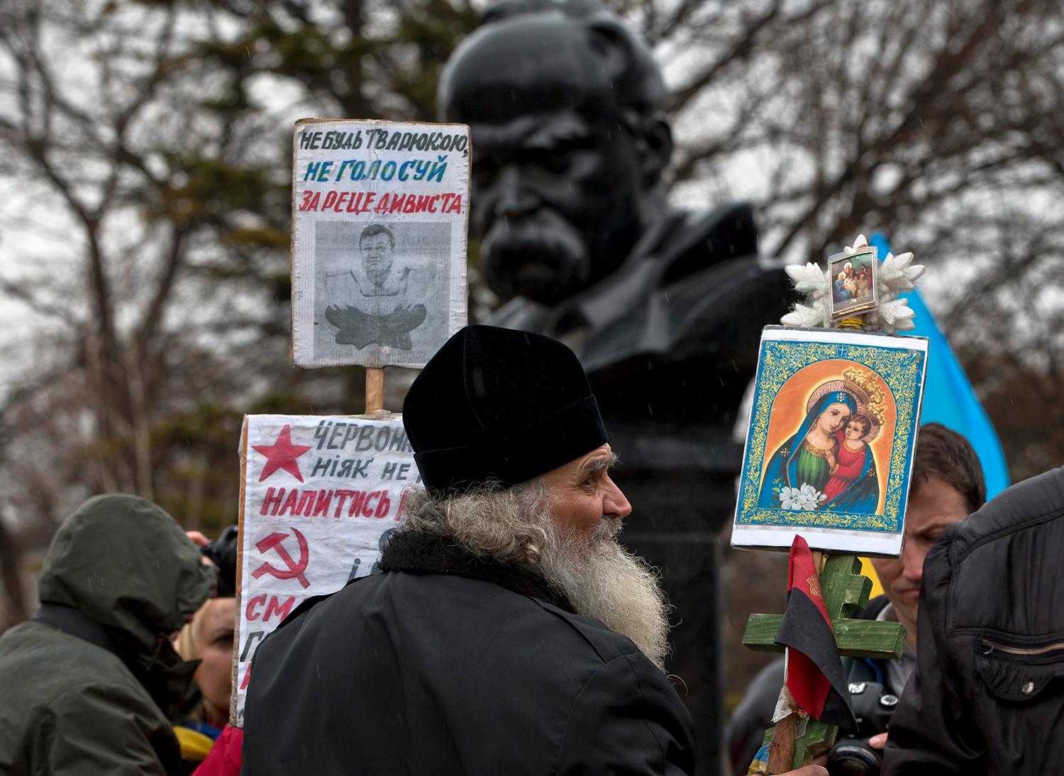 För Ukraina En ukrainsk-ortodox munk på en demonstration för att Krim ska tillhöra Ukraina i Simferopol fredag 7 mars. På plakatet står bland annat ”Rösta inte för brottslingen”, ”Röda stjärnan kräver mer blod” och ”Hammaren och skäran är död och hunger”.