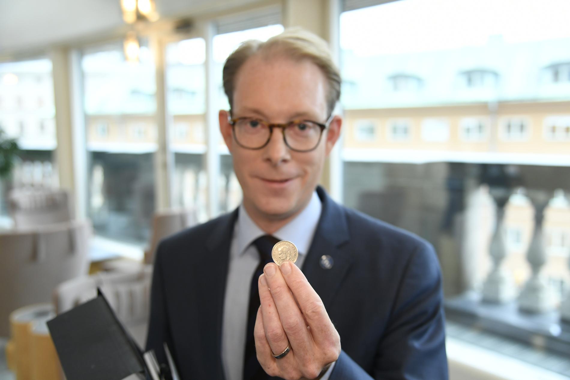 Tobias Billström håller upp myntet.