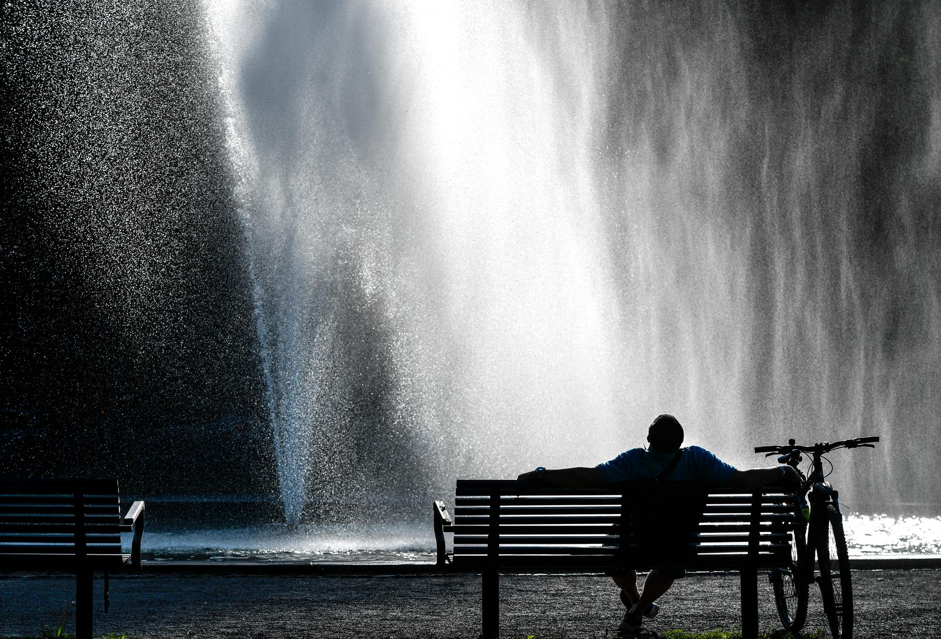 En man njuter av den tidiga sommarvärmen vid fontänen i Tessinparken i Stockholm.