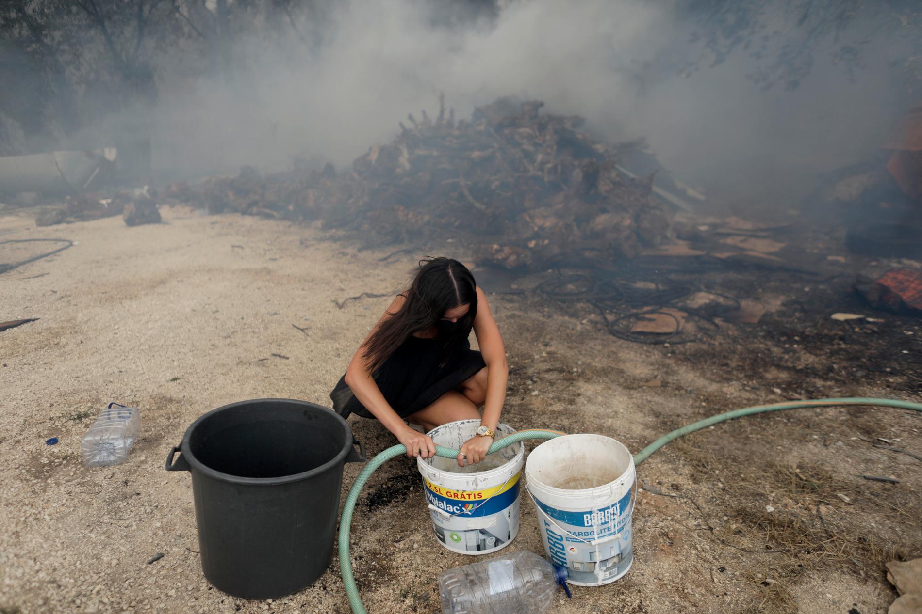 En kvinna fyller hinkar med vatten i Figueiras i Portugal, där invånarna försökte släcka en skogsbrand i tisdags. 