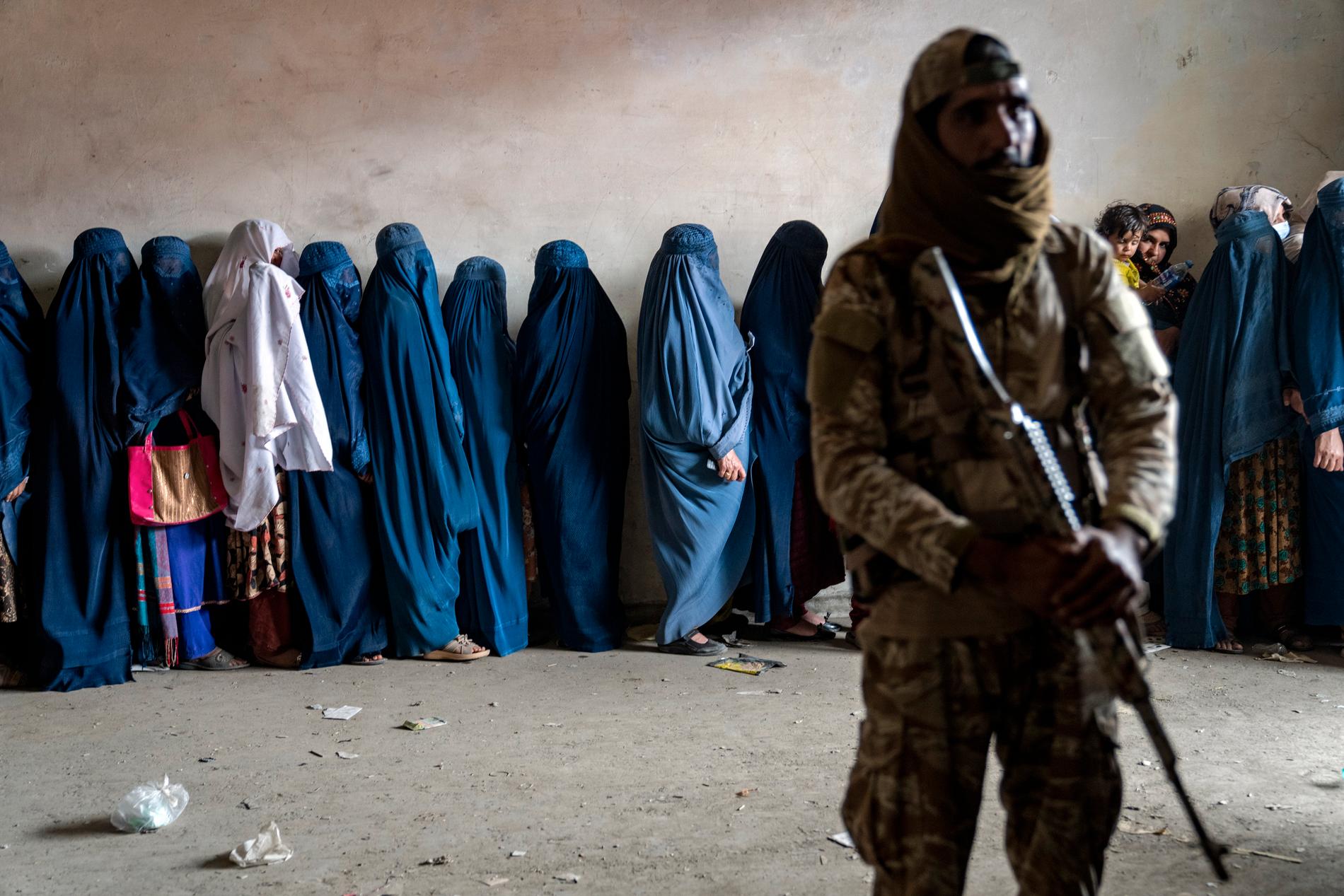 En taliban står vakt när kvinnor i Kabul köar för att ta emot matpaket från en biståndsorganisation. 