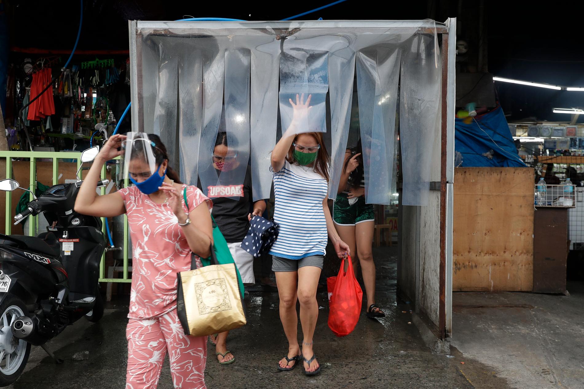 Kvinnor lämnar en desinfektionsstation efter att ha handlat mat på en marknad i staden Quezon. Arkivbild.