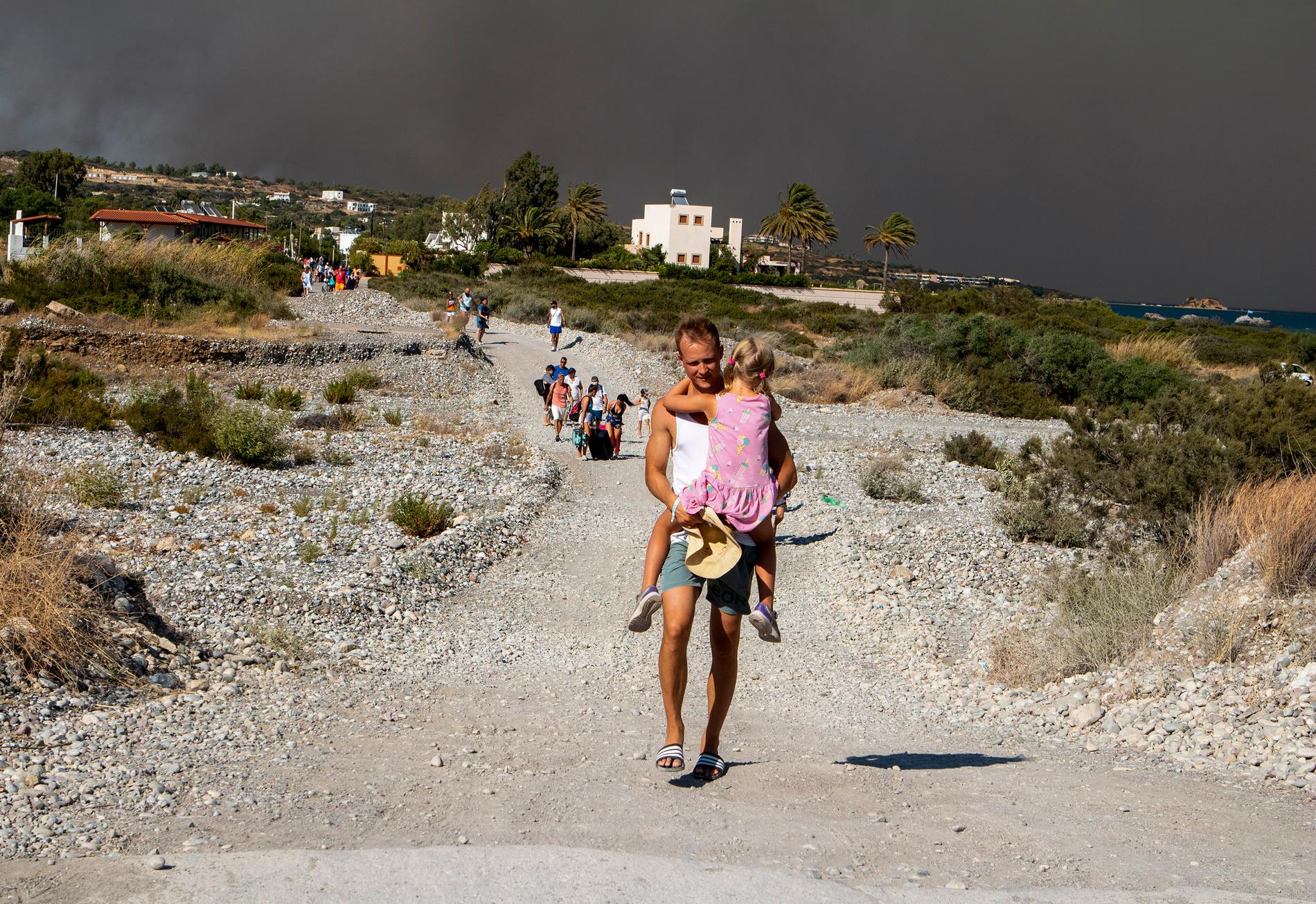 En turist bär sitt barn bort från ett brandområde på den grekiska semesterön Rhodos under lördagen.