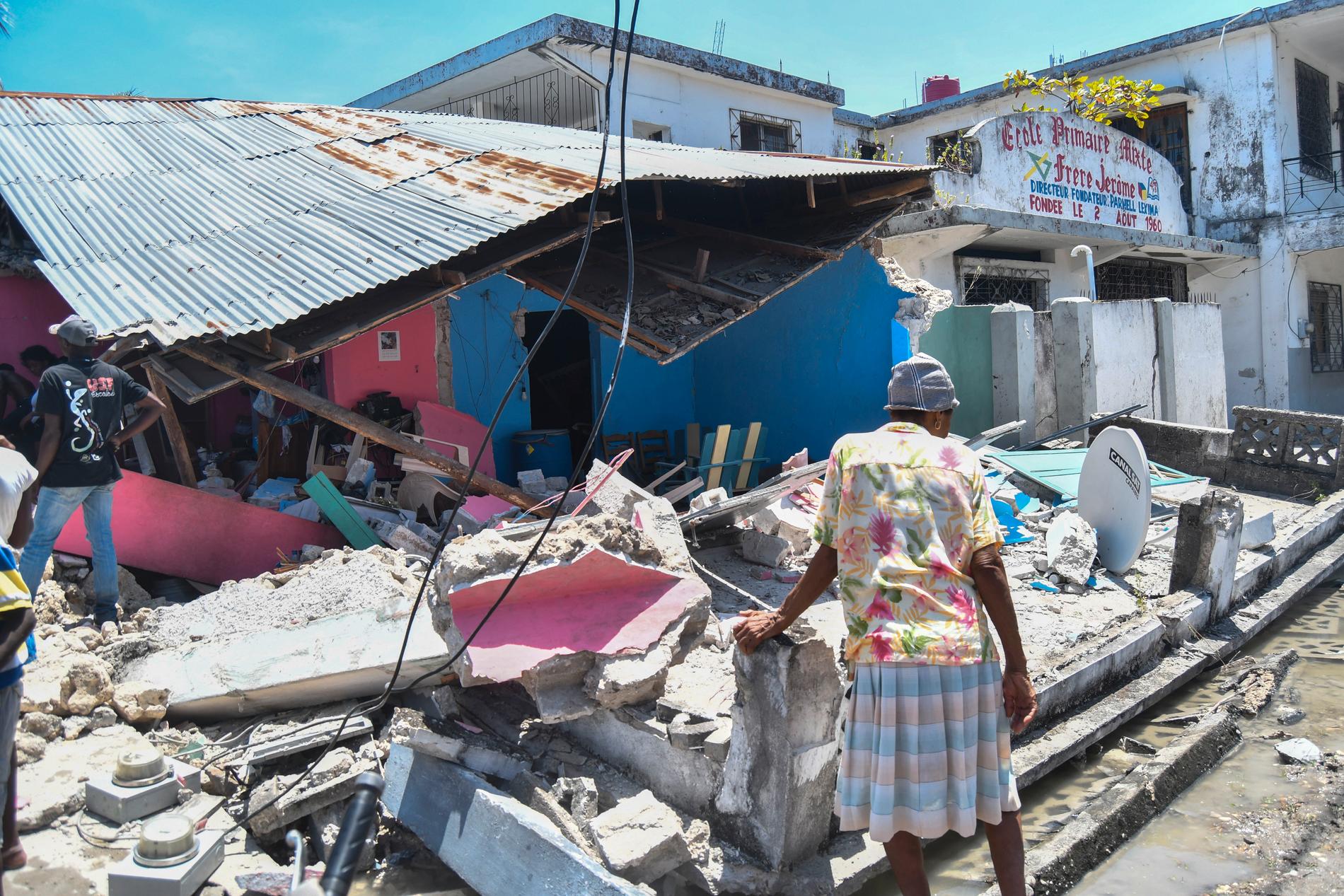 En kvinna framför ett totalförstört hem i Haiti.