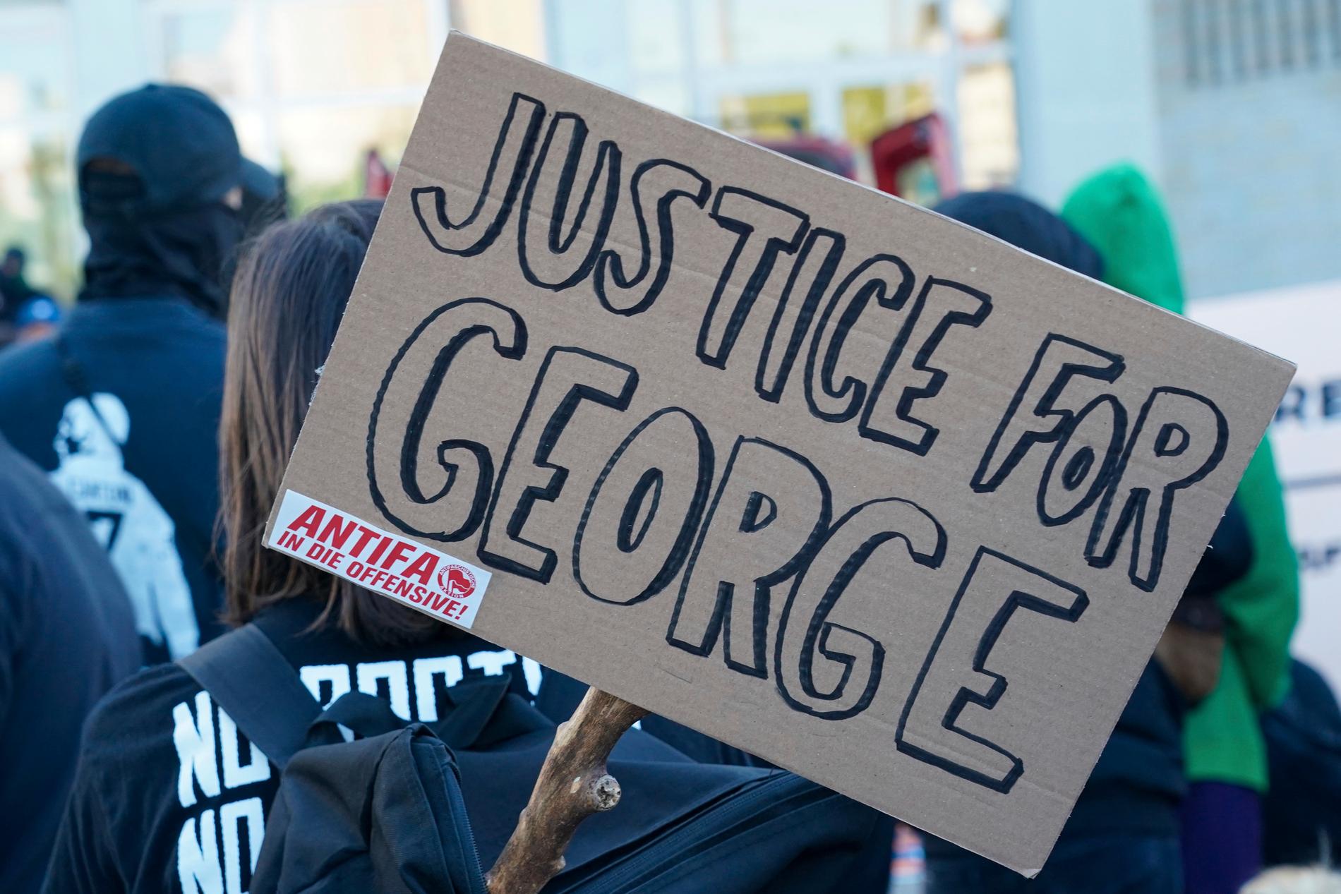 En skylt med texten "Rättvisa för George" (som syftar på George Floyd som dödades i ett brutalt polisingripande) och ett klistermärke med texten "Antifa på offensiven" vid en tysk demonstration mot polisvåldet i USA.