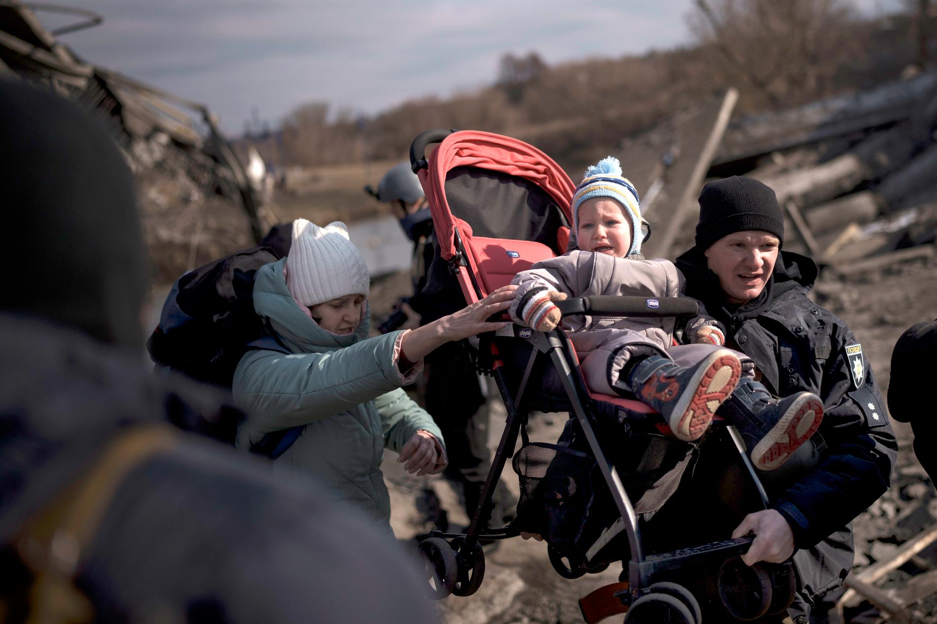 En man bär en barnvagn över bråte när de flyr Irpin i utkanten av Kiev. 