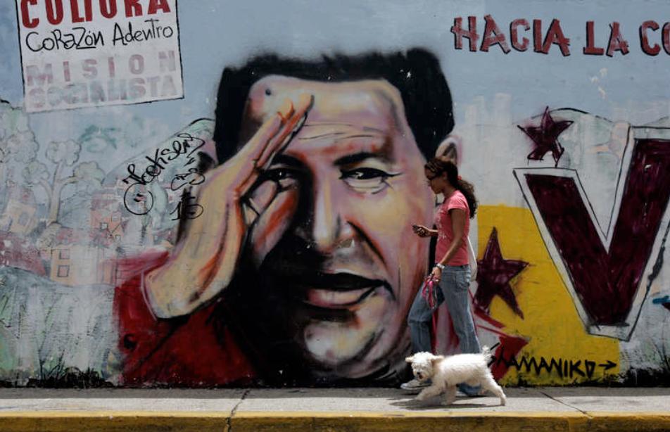 Finns överallt En kvinna och hennes hund passerar en av de många målningarna av Venezuelas president Hugo Chavez.