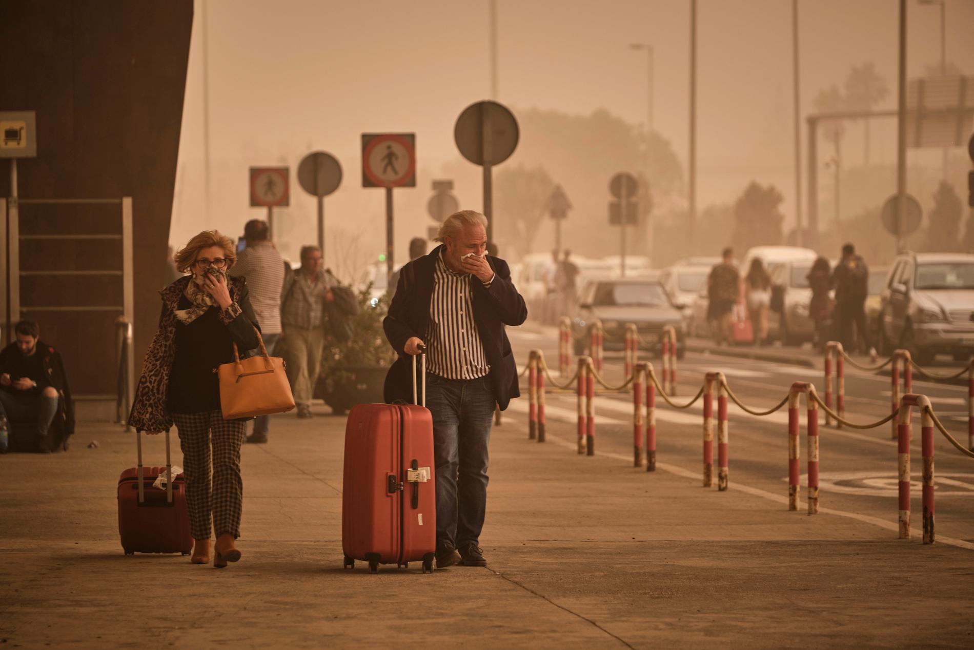 Två resenärer skyddar näsa och mun mot sanden vid flygplatsen på Teneriffa. 