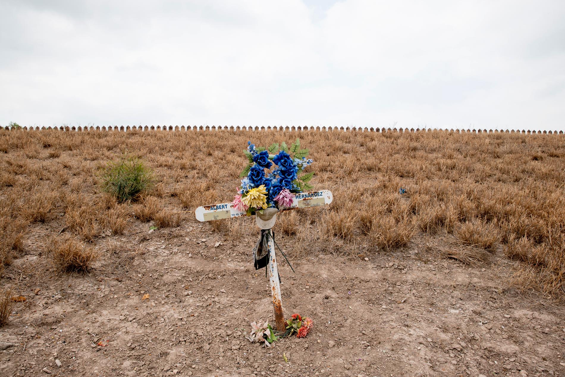 Ett kors markerar minnesplatsen för en död migrant. I bakgrunden skymtar en del av stålbarriären som delar USA och Mexiko.
