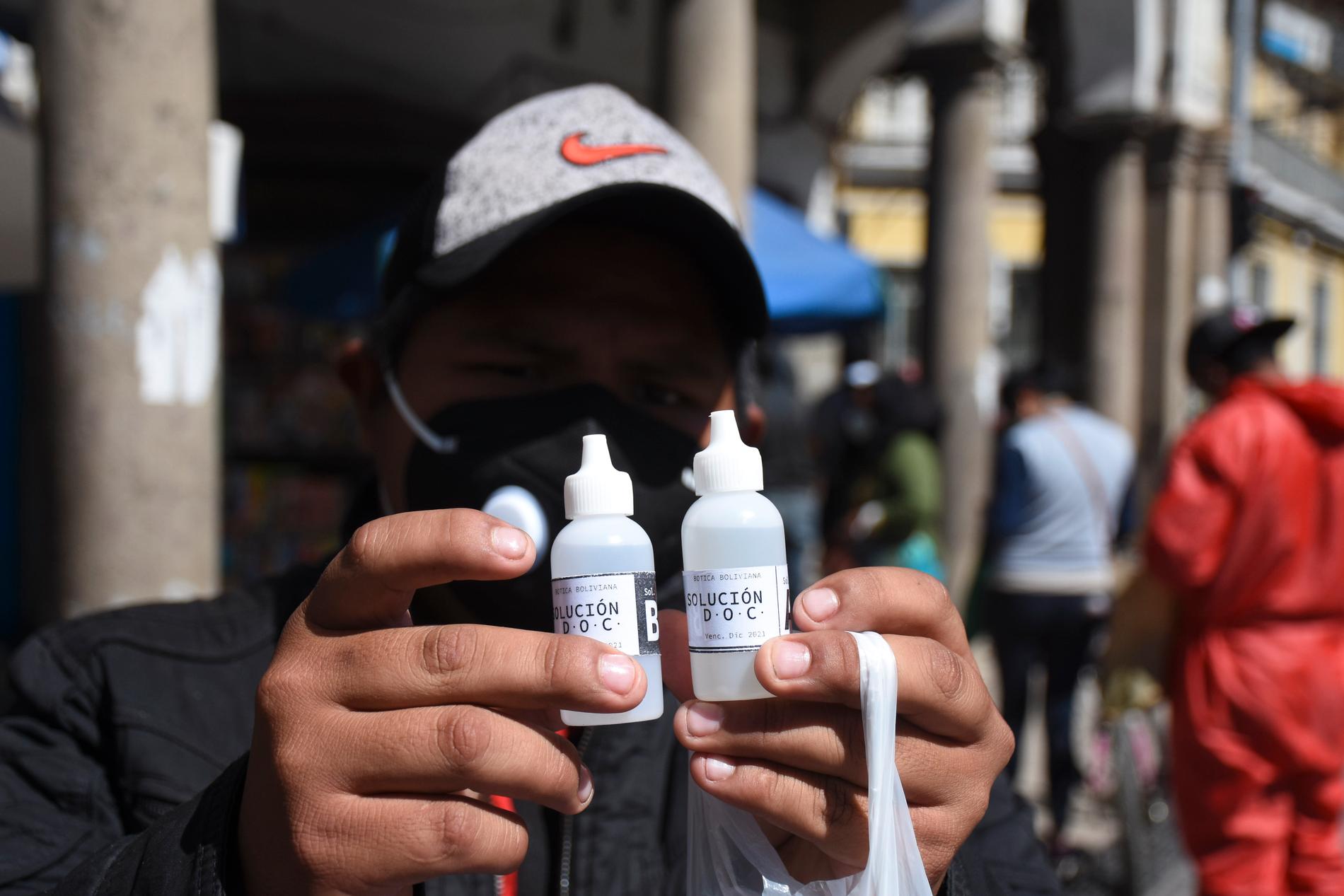 En man håller upp två flaskor klordioxid som han har köpt på ett apotek i Cochabamba i Bolivia.