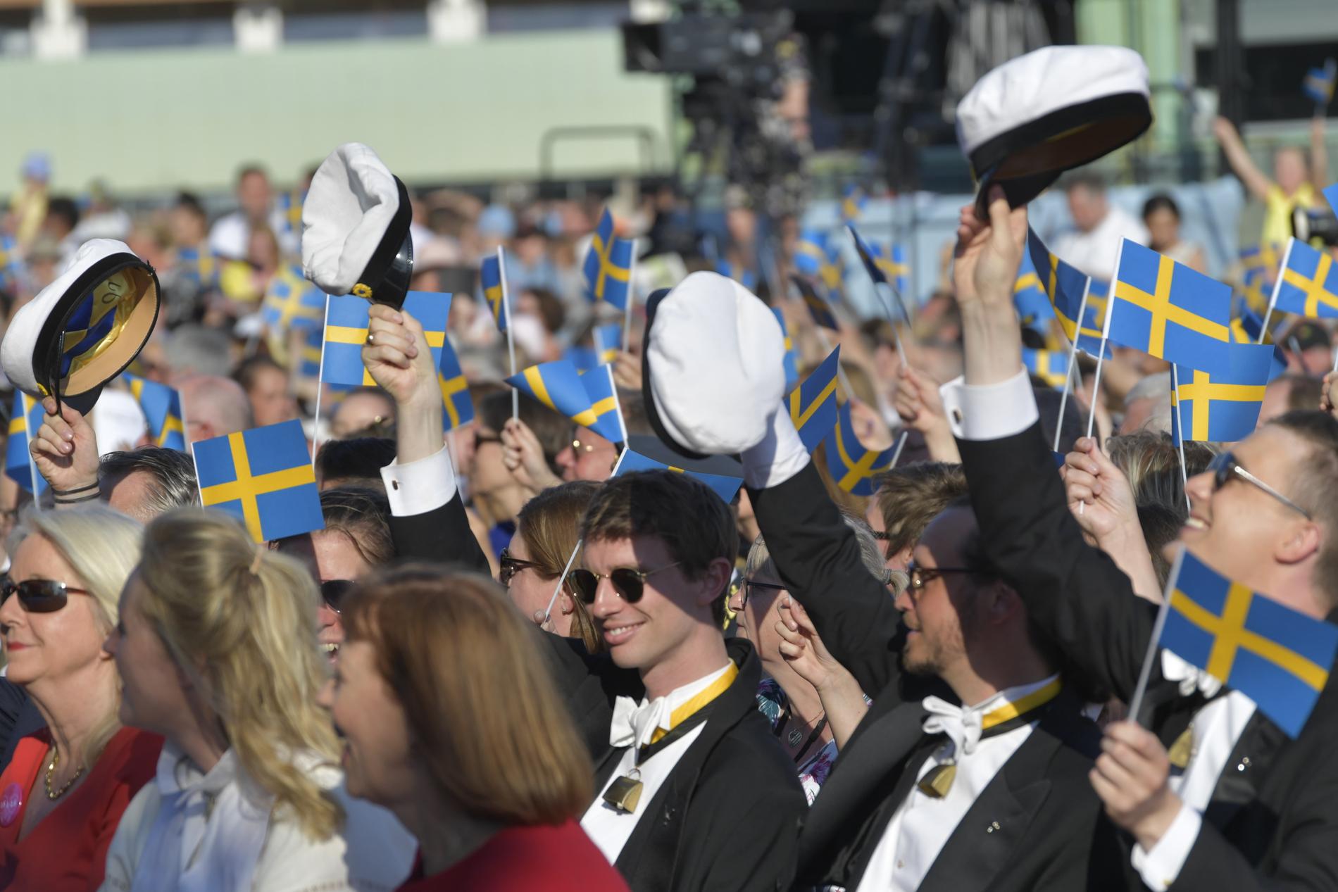 Besökare viftar med svenska flaggor och studenter med studentmössor på Skansen.
