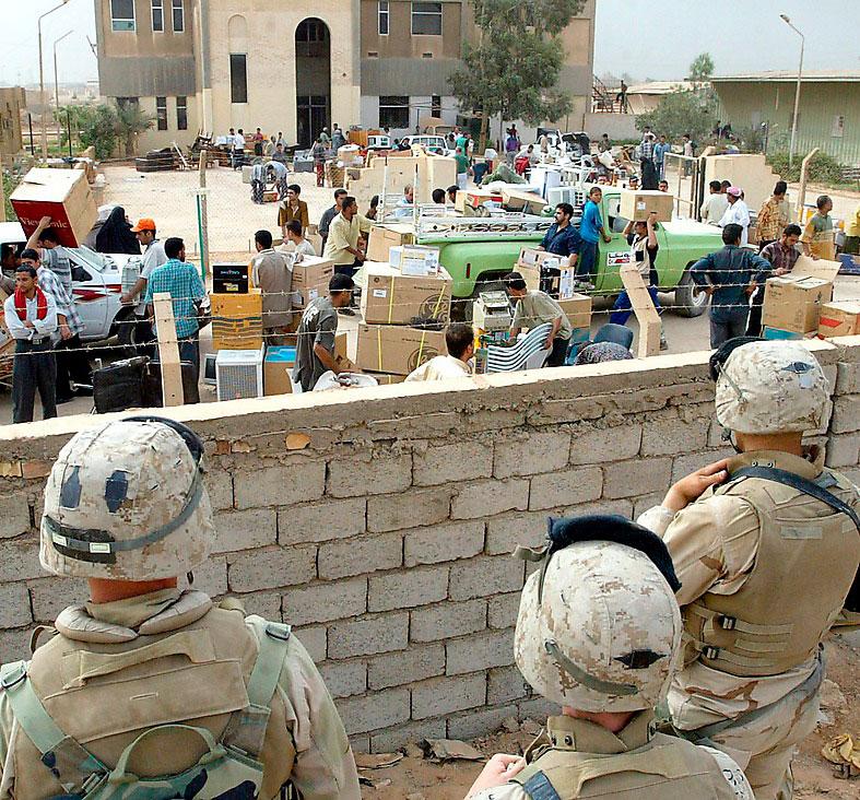 Amerikanska soldater tittar på medan en myndighetsbyggnad plundras i Bagdad.