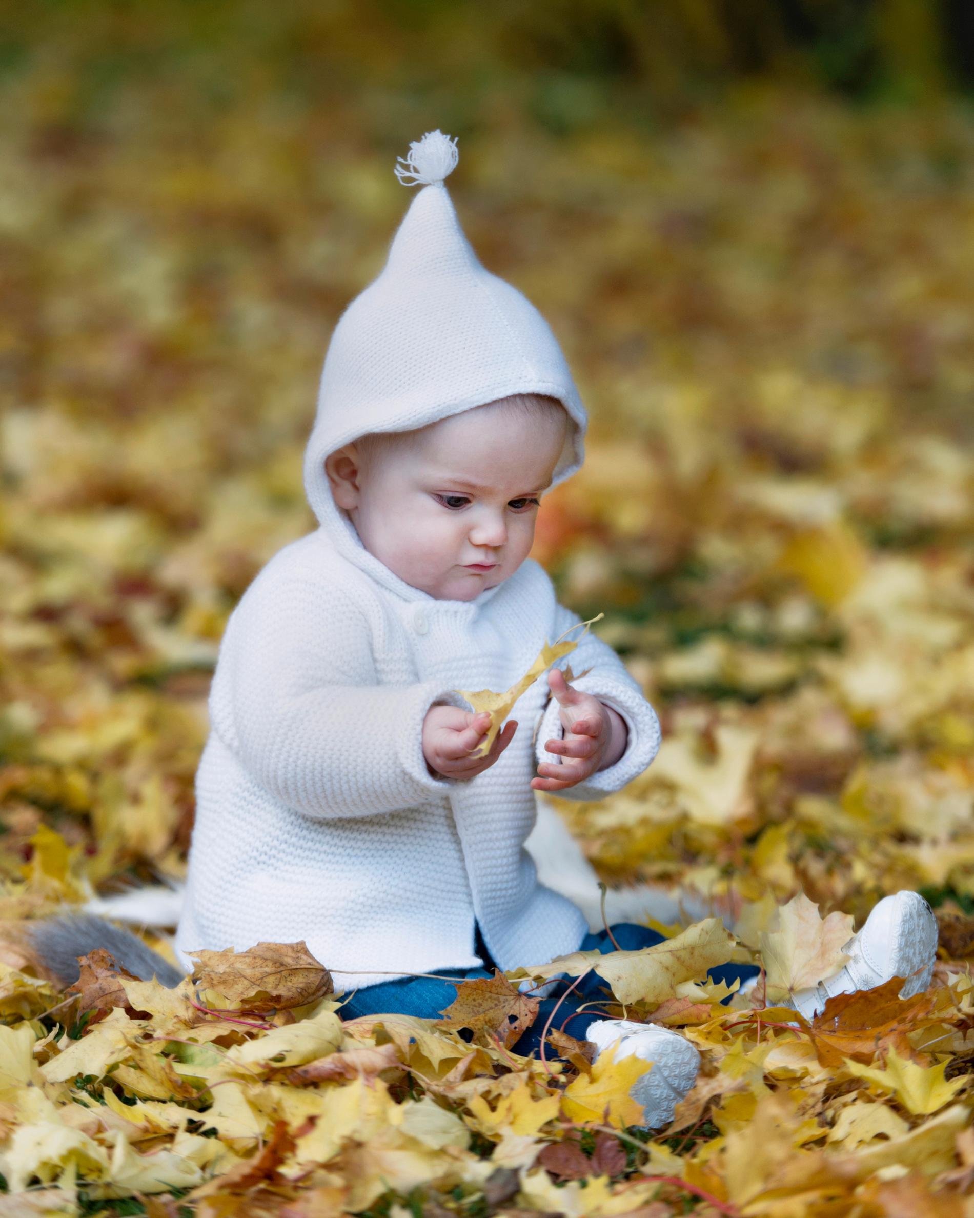 Vad kul det är att leka med löv! Den halvåret gamla Estelle fortsätter med sin favoritaccessoar – huvan– i favoritfärgen vitt.