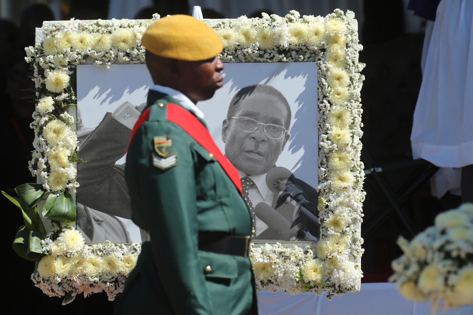 En soldat vid ett porträtt av den tidigare presidenten Robert Mugabe vid begravningen i höstas. Arkivbild.