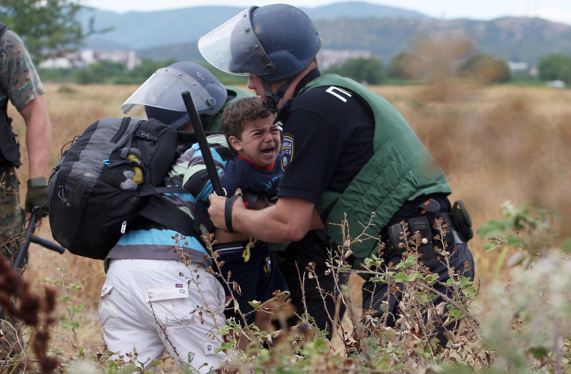 En flykting med ett barn försöker ta sig över gränsen mellan Makedonien och Grekland.