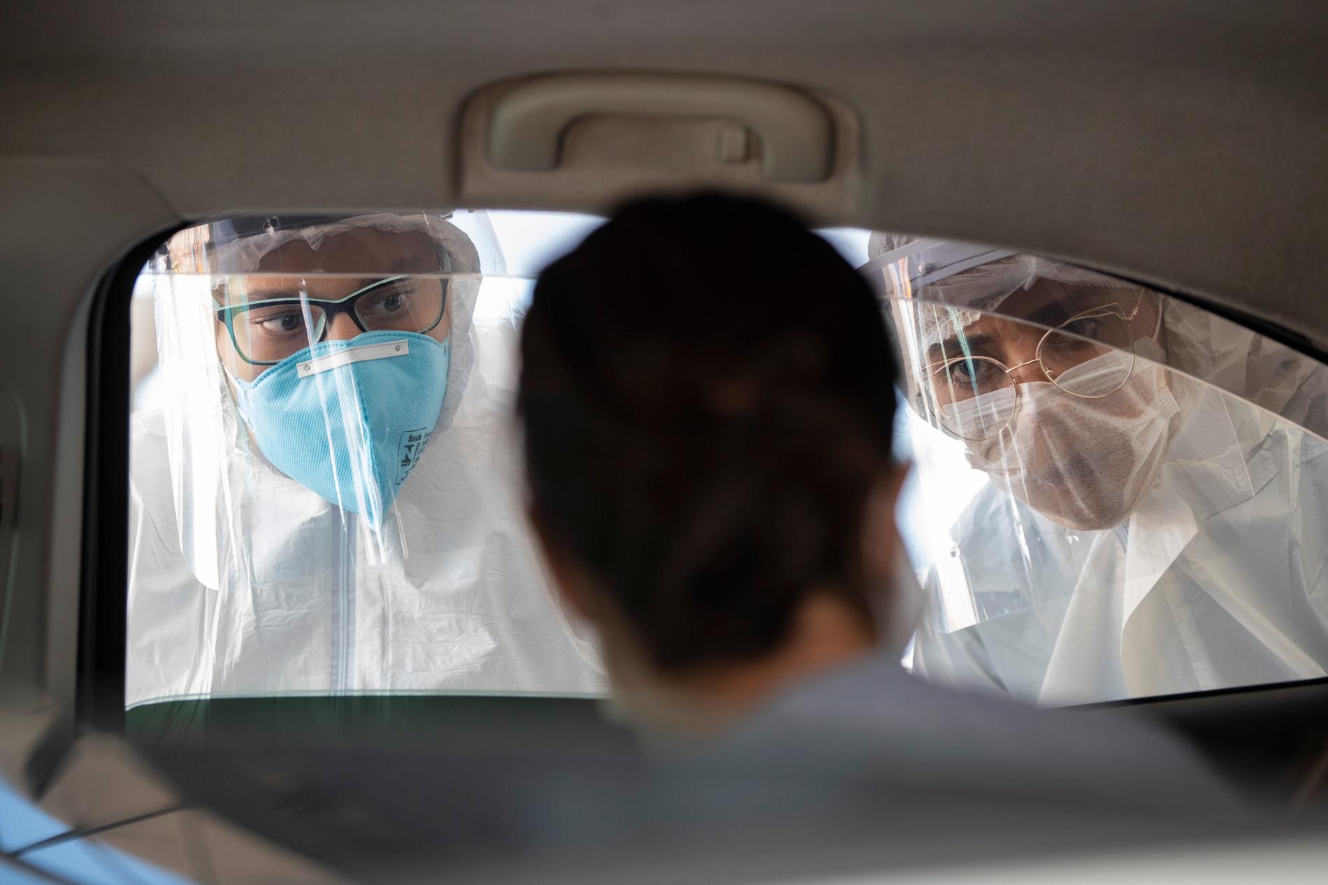 Vårdpersonal undersöker människor genom fönstret på en bil utanför São Paulo för att se om de uppvisar några symtom.