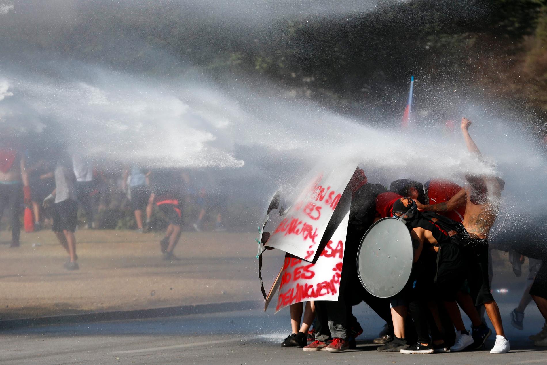 Regimkritiska demonstranter står emot trycket från vattenkanonerna i Chiles huvudstad Santiago den 15 november.