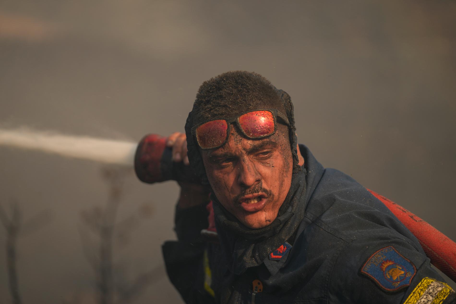 En brandman sprutar vatten i försök att stoppa brand vid berget Penteli, Grekland, 19 juli 2022.