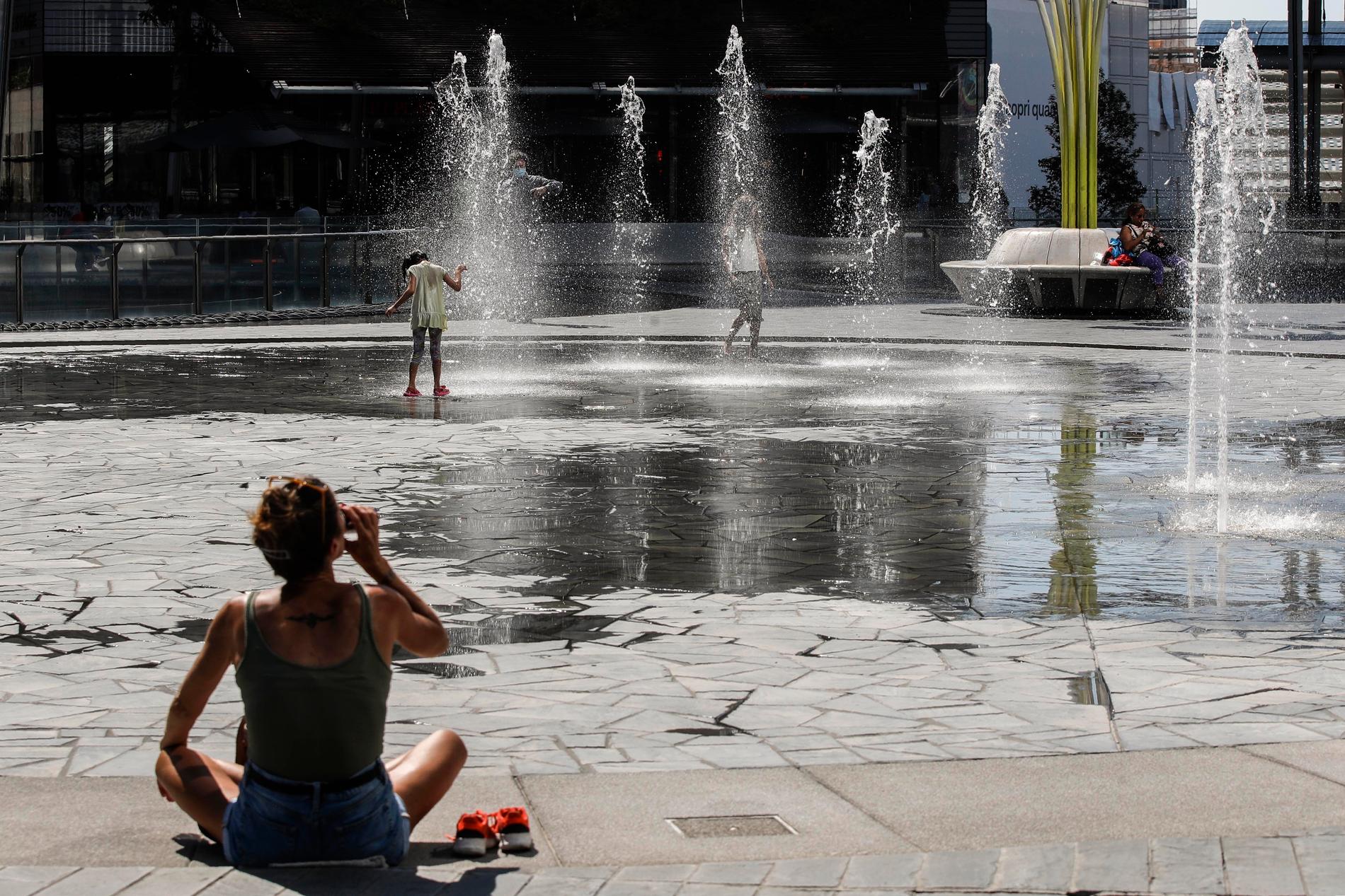 Barn svalkar sig i en fontän i Milano under värmeböljan.