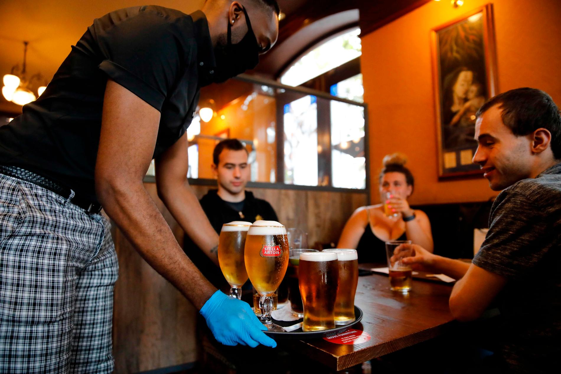 Sittande kunder serveras av personal med munskydd och plasthandskar på Wetherspoon pub i London.