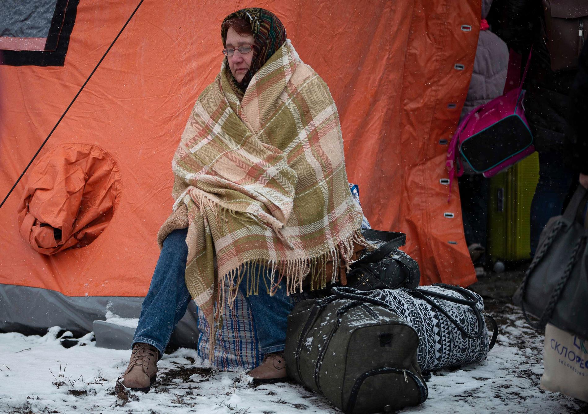 En kvinna som flytt Ukraina försöker hålla värmen med en filt utanför ett tält vid Medyka, Polen. 