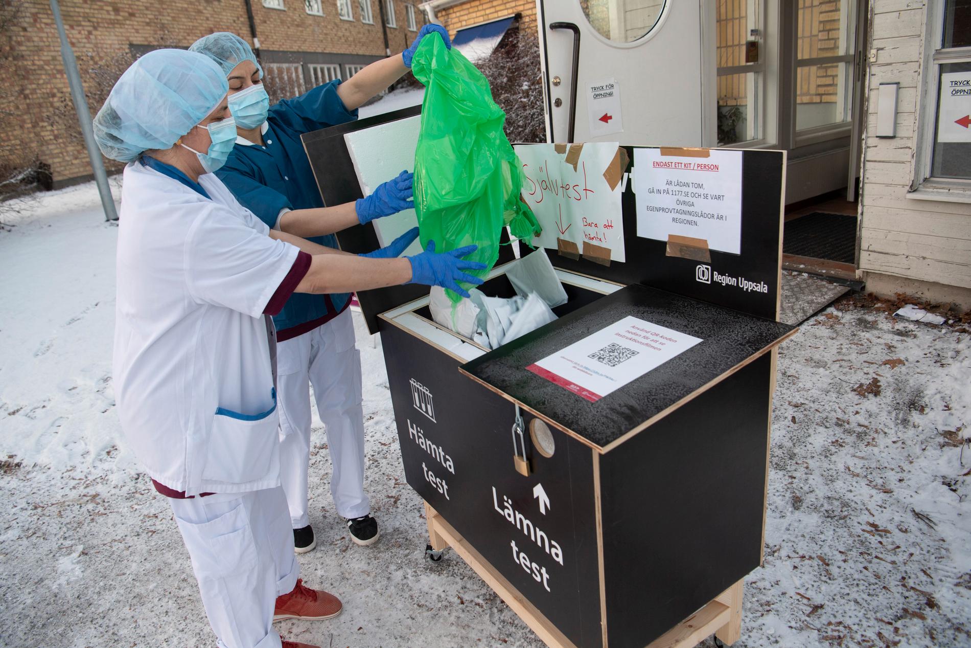 Undersköterskan Seema Gul, närmast i bild, fyller på förpackningar med covid-19-test i självbetjäningslådan utanför lasarettet i Enköping. På måndagen hämtades 840 tester ur lådan.