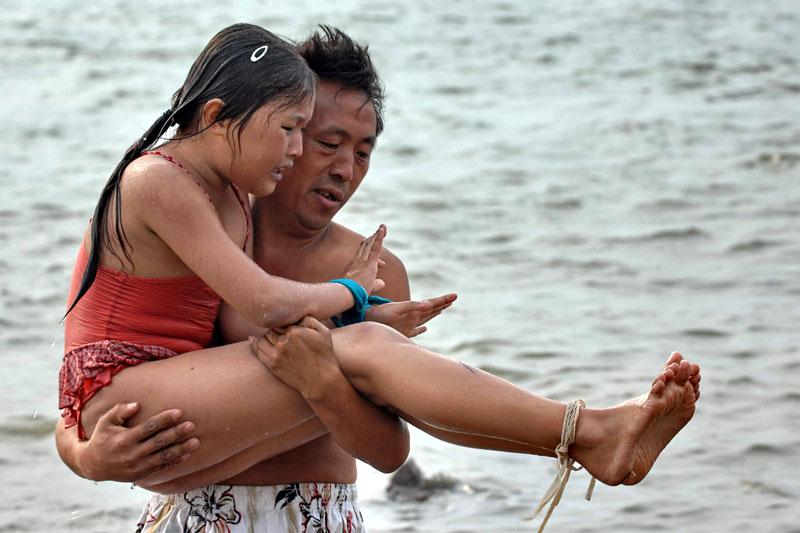 Behöver hjälp efteråt Vattnet var kallt när 10-åriga Huang Li simmade. Tre timmar senare hjälper pappa Huang Daosheng henne upp ur vattnet.