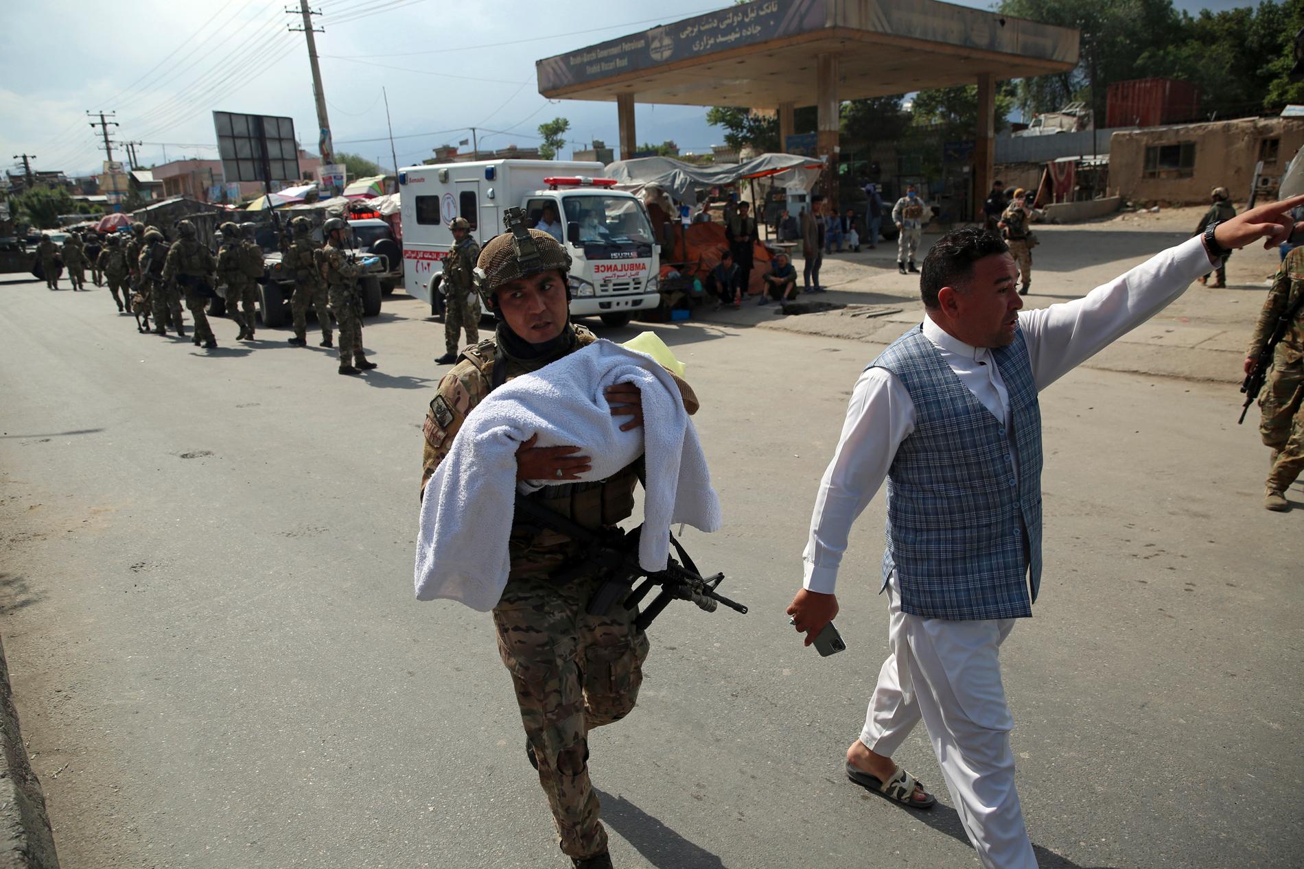En afghansk soldat bär på ett barn efter att beväpnade män angripit en förlossningsklinik i Kabul i tisdags.