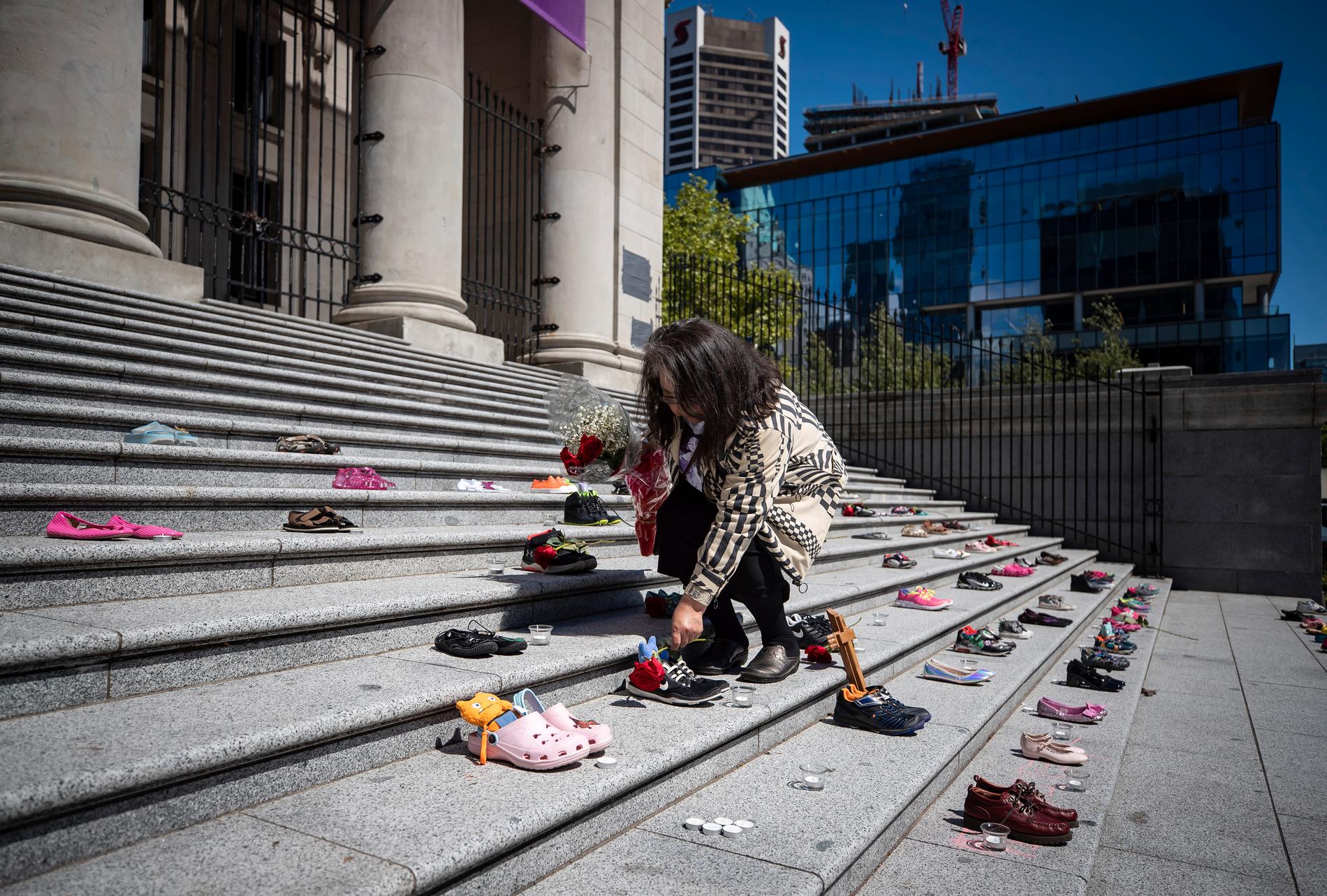 Delhia Nahanee, som tillhör folkgruppen Squamish, placerar en ros på en av de 215 par barnskor som har placerats ut på trappan till Vancouver Art Gallery till minne av de barn vars kvarlevor har hittats på den tidigare internatskolan Kamloops i British Columbia.