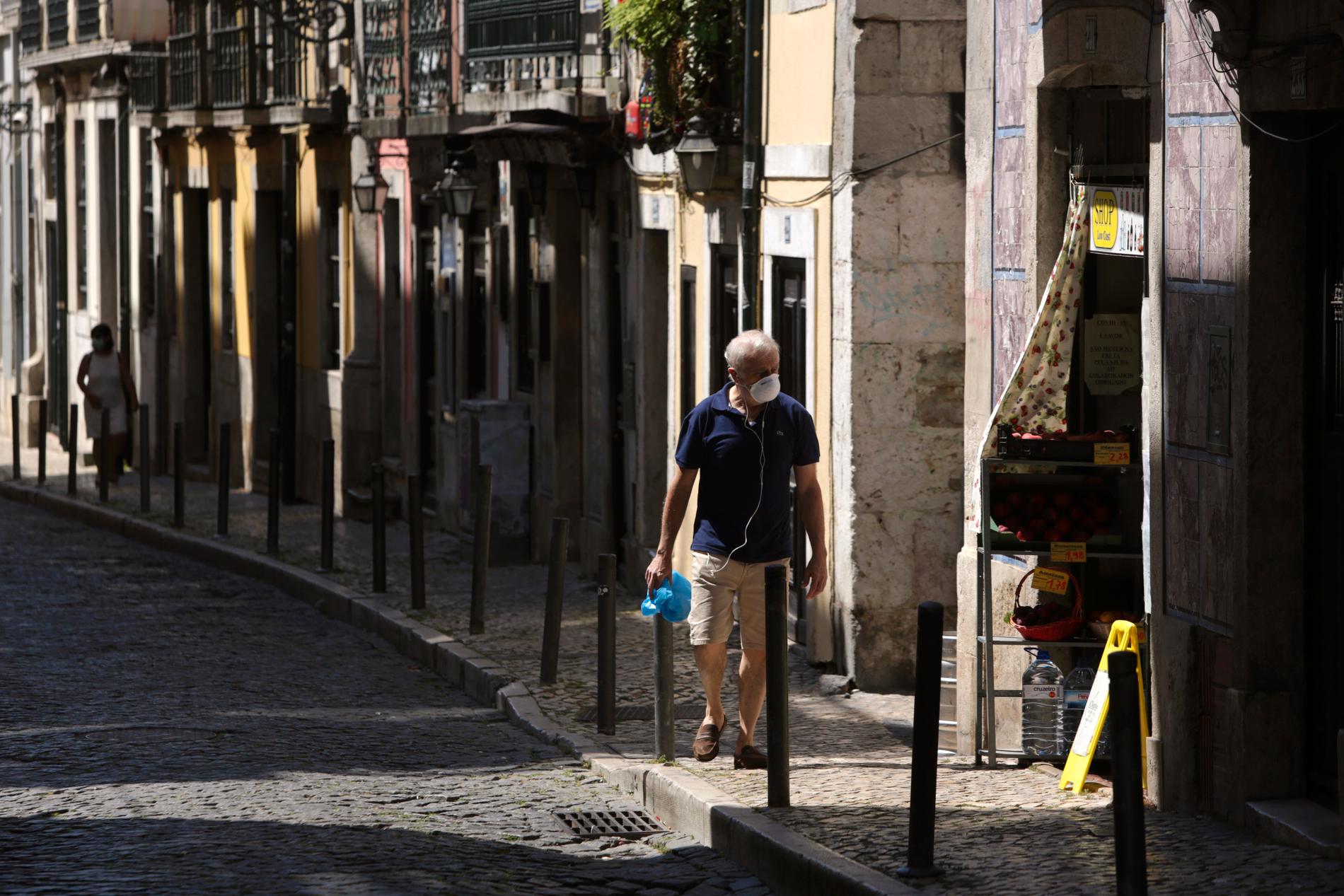 En man iförd munskydd promenerar längs en gata i Portugals huvudstad Lissabon. Arkivbild.