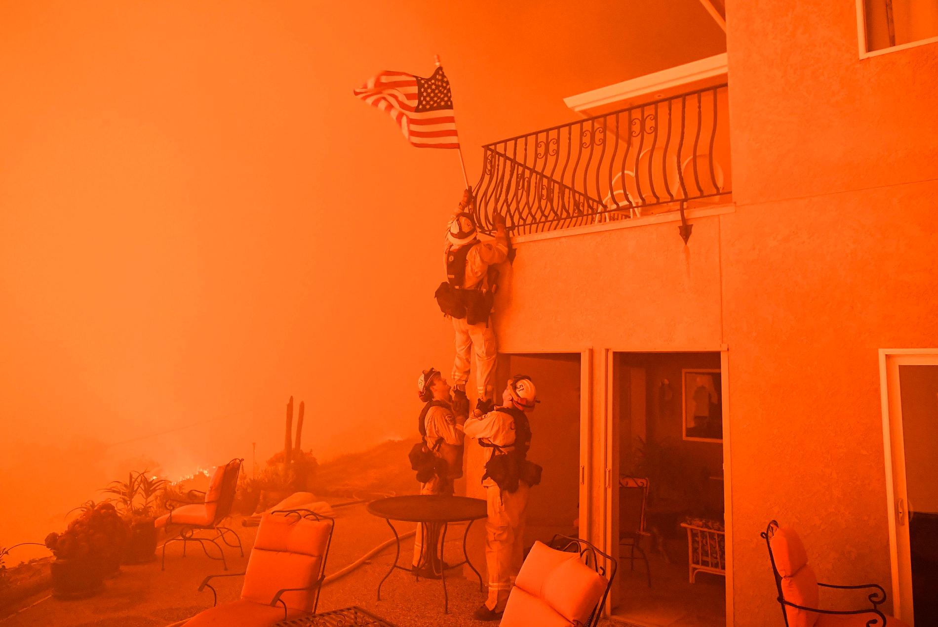 Brandmän tar ned en flagga när elden närmar sig ett hem i Oroville. Flera skogsbränder härjar i Kalifornien, USA och mer än 2000 brandmän deltar i släckningsarbetet.