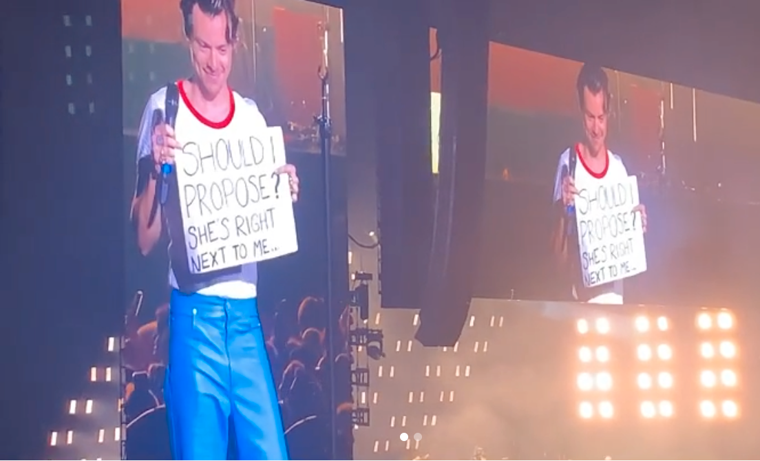 Harry Styles håller upp skylten på scen i Tele2 arena. 