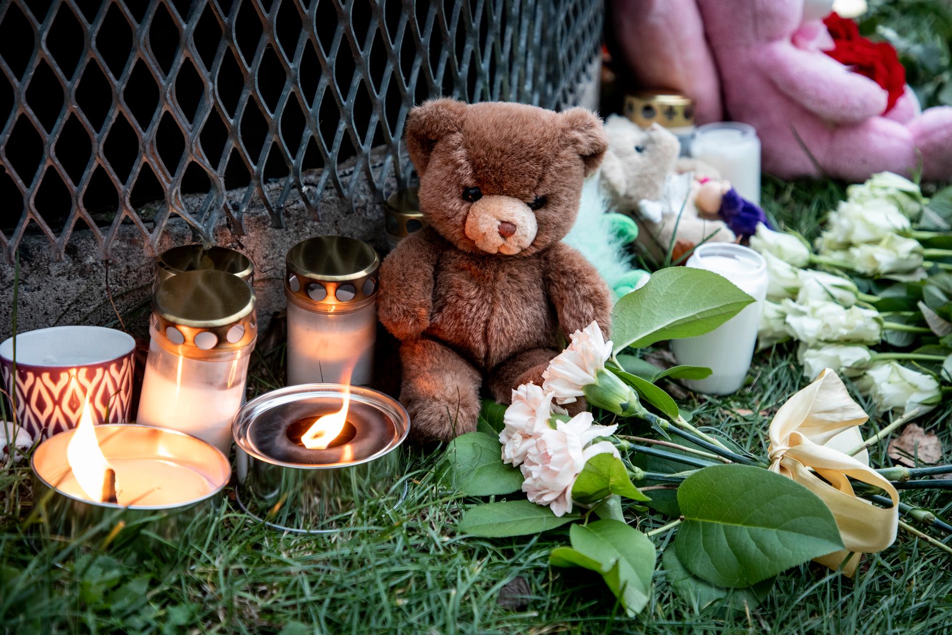 Gosedjur, blommor och ljus har lagts ner vid den plats där två barn hittades mycket svårt skadade utanför ett bostadshus i Hässelby på söndagskvällen. Ett av barnen avled senare.