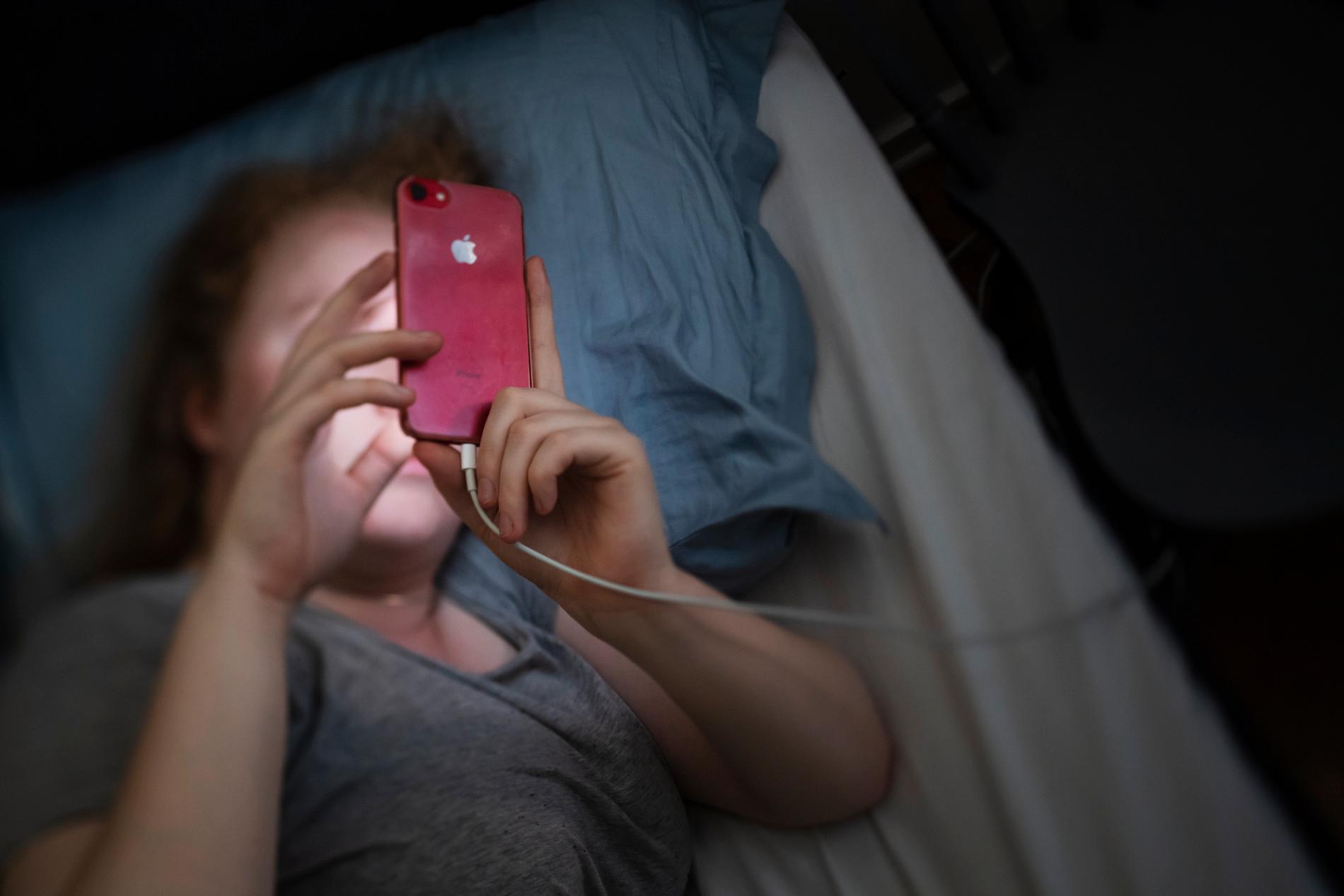 En kvinna tittar på mobilen mitt i natten. Genrebild.