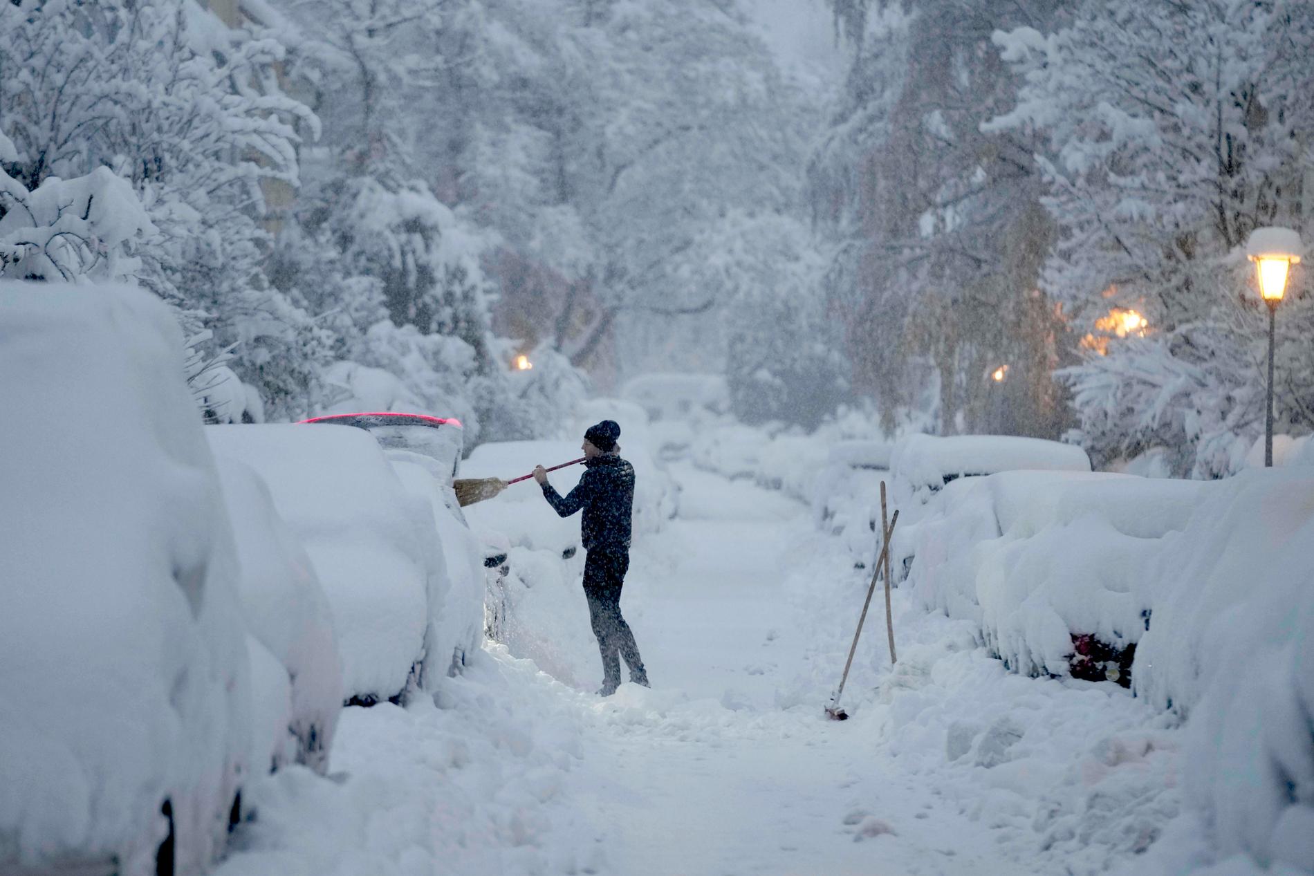 En man i München tar bort snö från sin bil.
