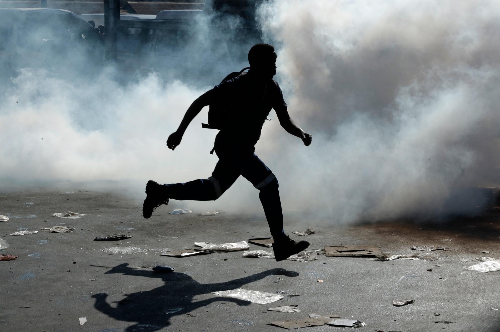 En man springer bort från tårgas i samband med att en butik plundrats i Germiston, öster om Johannesburg, i förra veckan.
