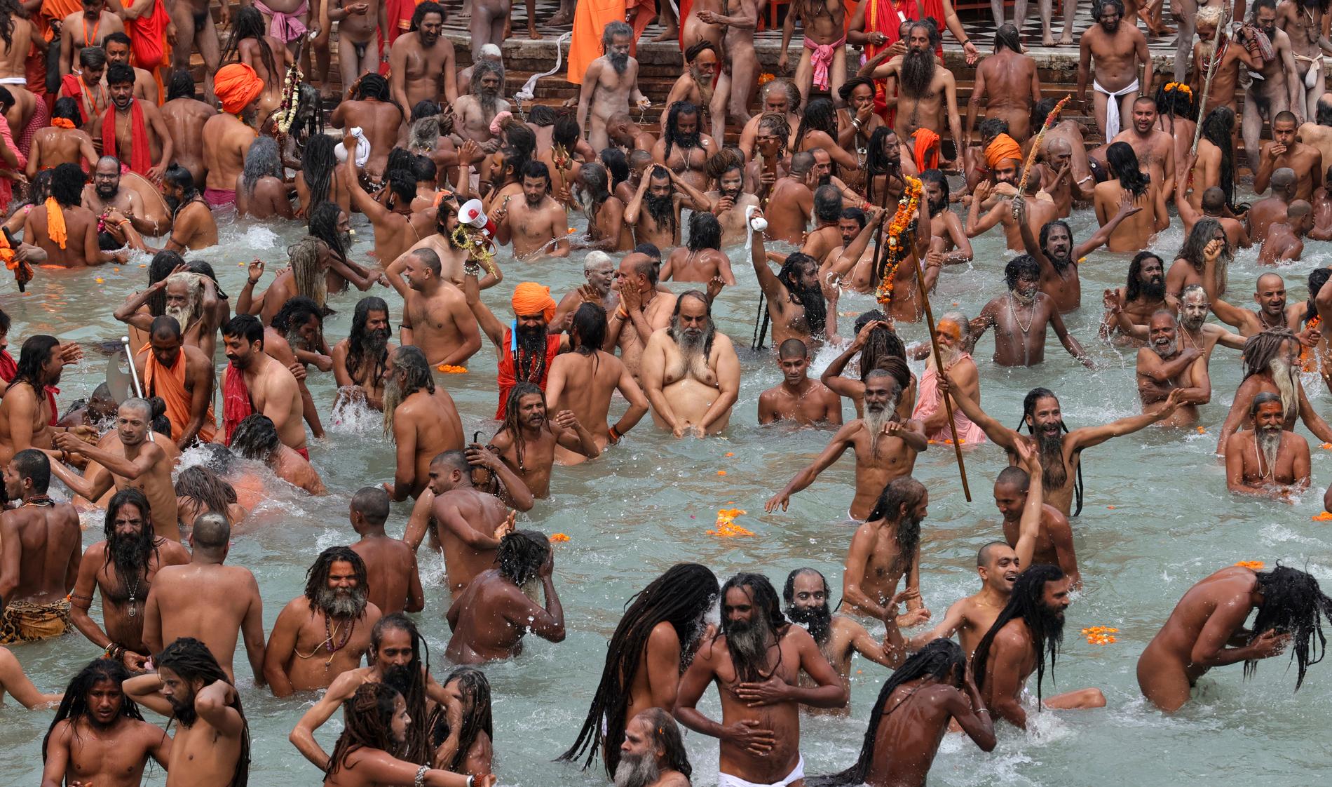 Troende – de flesta utan munskydd – firar den hinduiska högtiden kumbh mela genom att ta renande bad i floden Ganges.