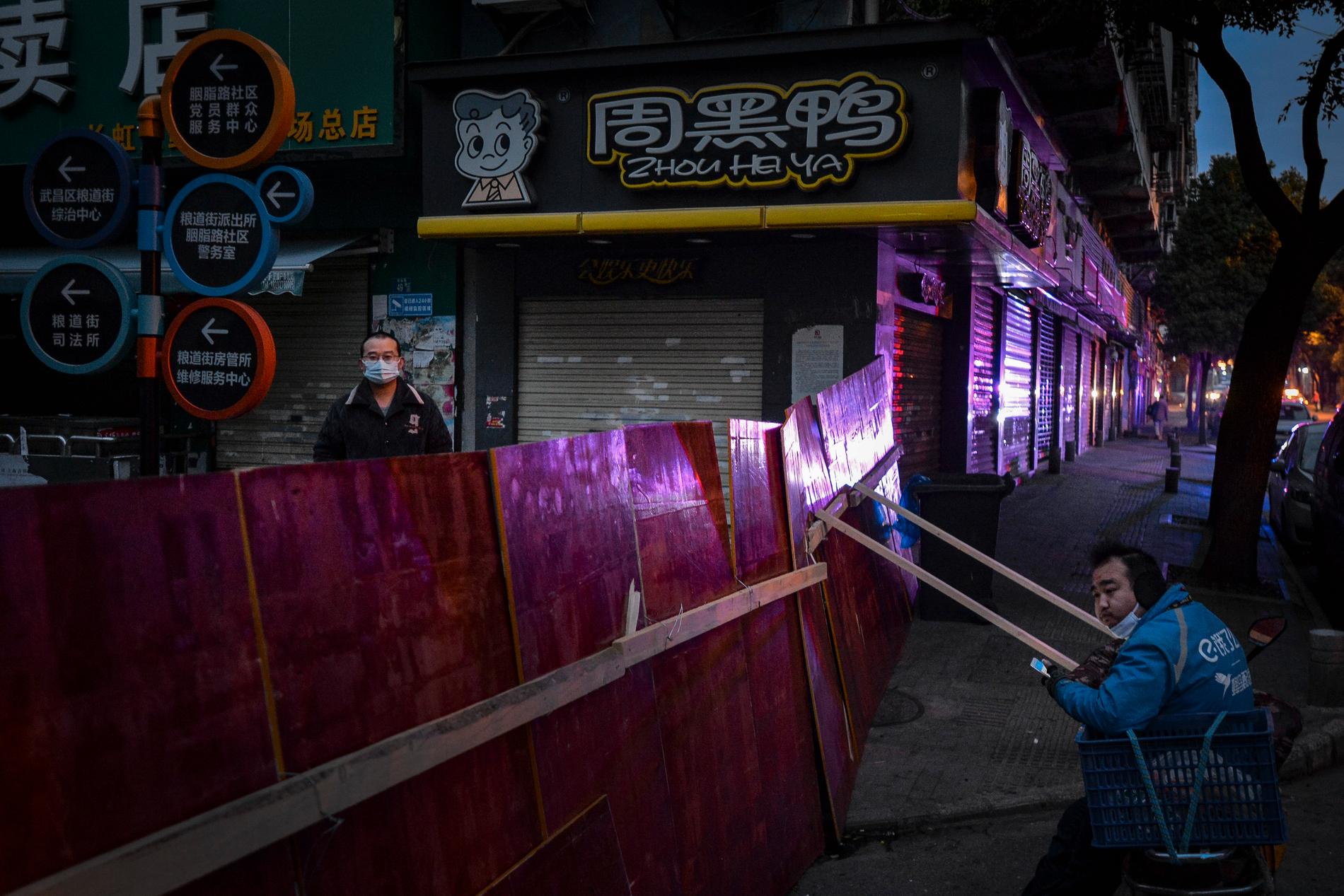 Två män väntar vid ett staket vid stängda affärer i Wuhan, i slutet av februari. Arkivbild.
