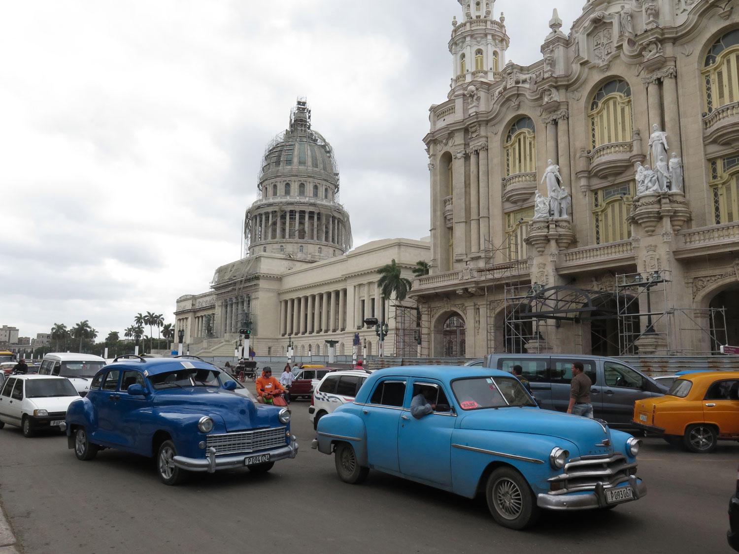 På Kuba är det bara Havanna som har tät trafik, som här framför Stora teatern och Capitolium, båda under renovering. Den ljusblå bilen är en Plymouth från 1950 med mer renodlad grill än åren före och större emblem, och i nära originalskick. Den bakre mörkblå kan vara en Plymouth från 1946 , med gangsterkeps och takrelingar(!). Lägg märke till självmordsdörrarna bak, de försvann på nästa årsmodell. När originalgrillen försvann är mer osäkert.