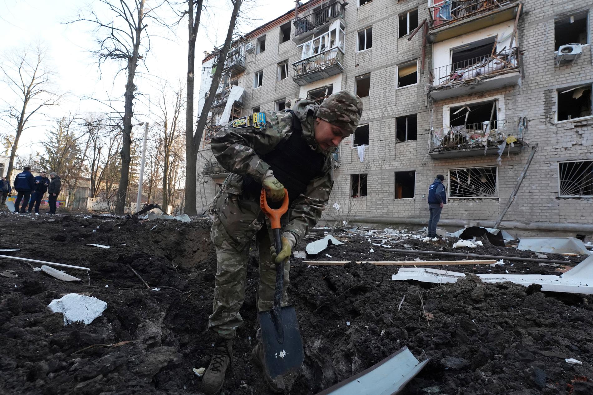 En polis framför ett förstört bostadshus i Charkiv.