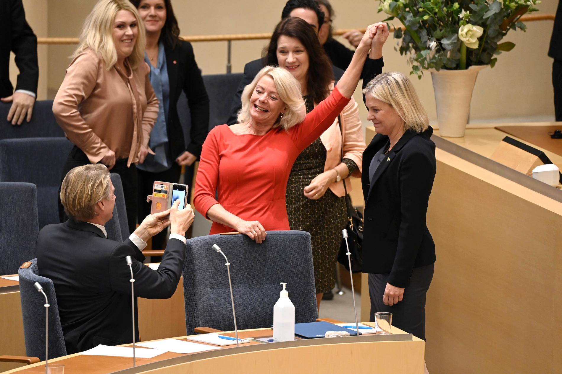Partikamraten Pia Nilsson gratulerar Magdalena Andersson efter att hon blivit vald till statsminister för andra gången. Miljöpartiets språkrör Per Bolund dokumenterar det historiska ögonblicket. 