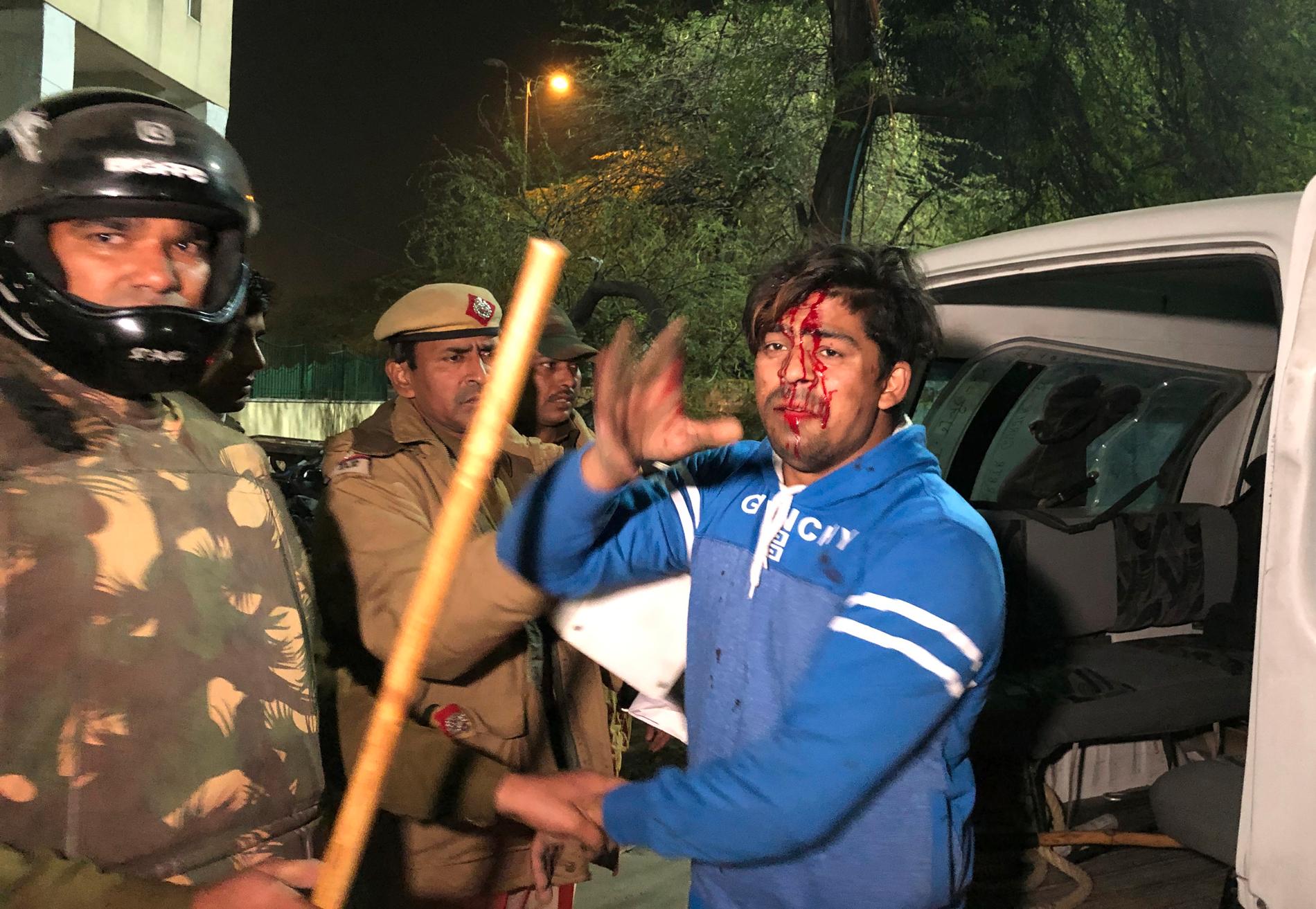 Polis griper en skadad student utanför universitetet Jamia Millia Islamia i Delhi, Indien. Bild tagen söndag 15 december.